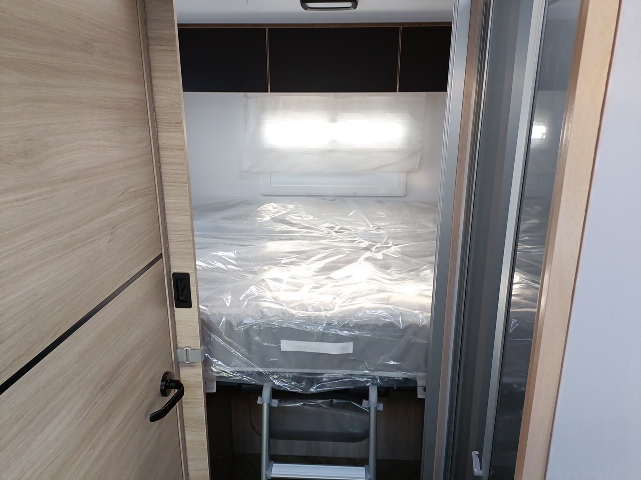 Peek inside an RV rental bedroom with a plastic-wrapped bed, window, and cabinet.. Challenger 384 Family 2024