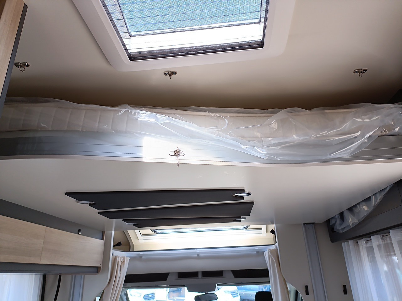 Inside this RV rental: an overhead bunk with a new, plastic-covered mattress, illuminated by a large ceiling skylight.. Itinéo PS 700 2024