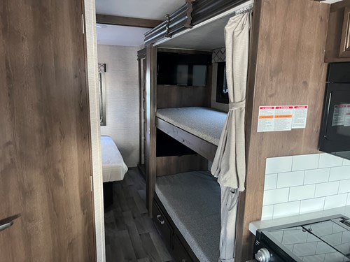 Inside an RV rental, showing a set of bunk beds, a compact kitchen with a stove, and a glimpse into an adjacent room.. Jayco Alante 2022