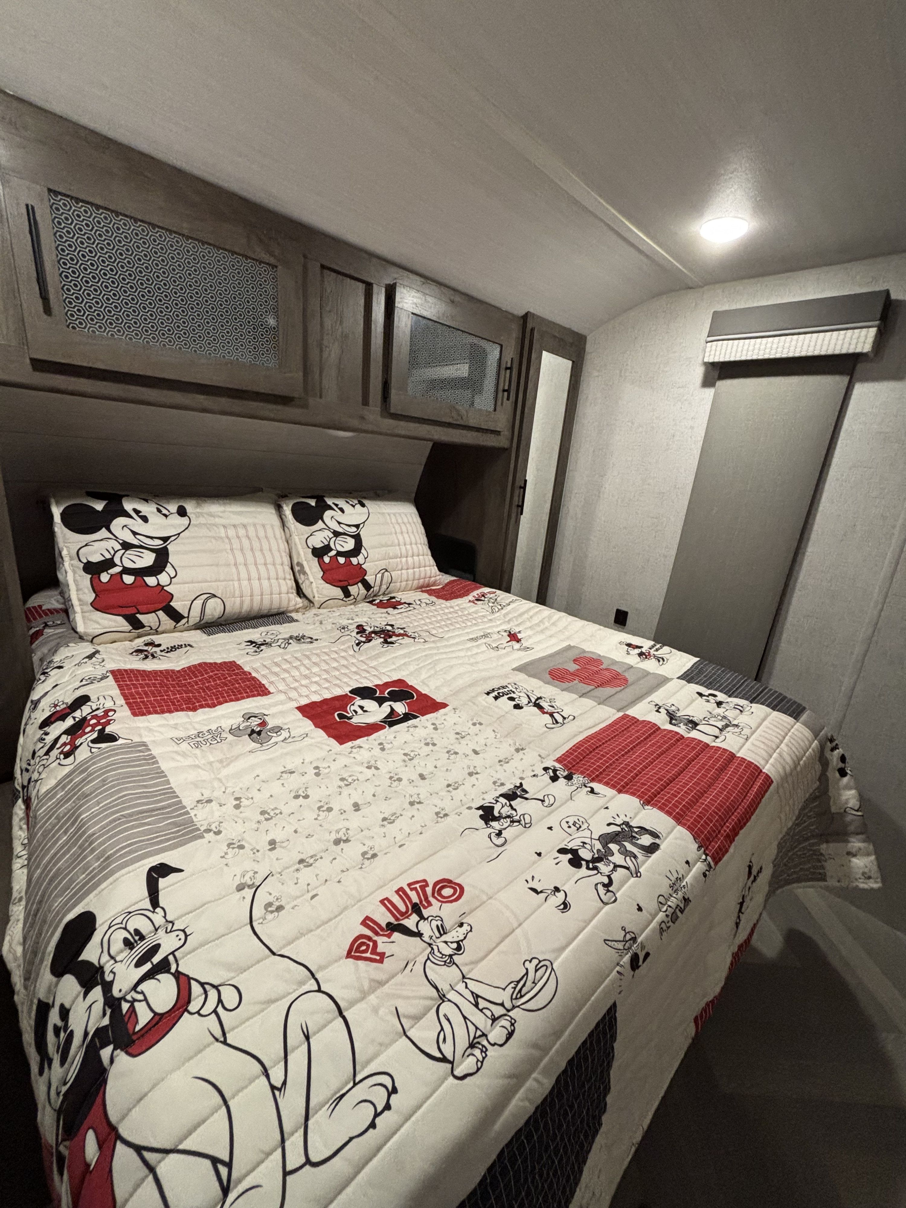 Cozy RV rental bedroom with Mickey Mouse bedding and storage cabinets, offering a fun, themed interior.. Forest River Wildwood 2021