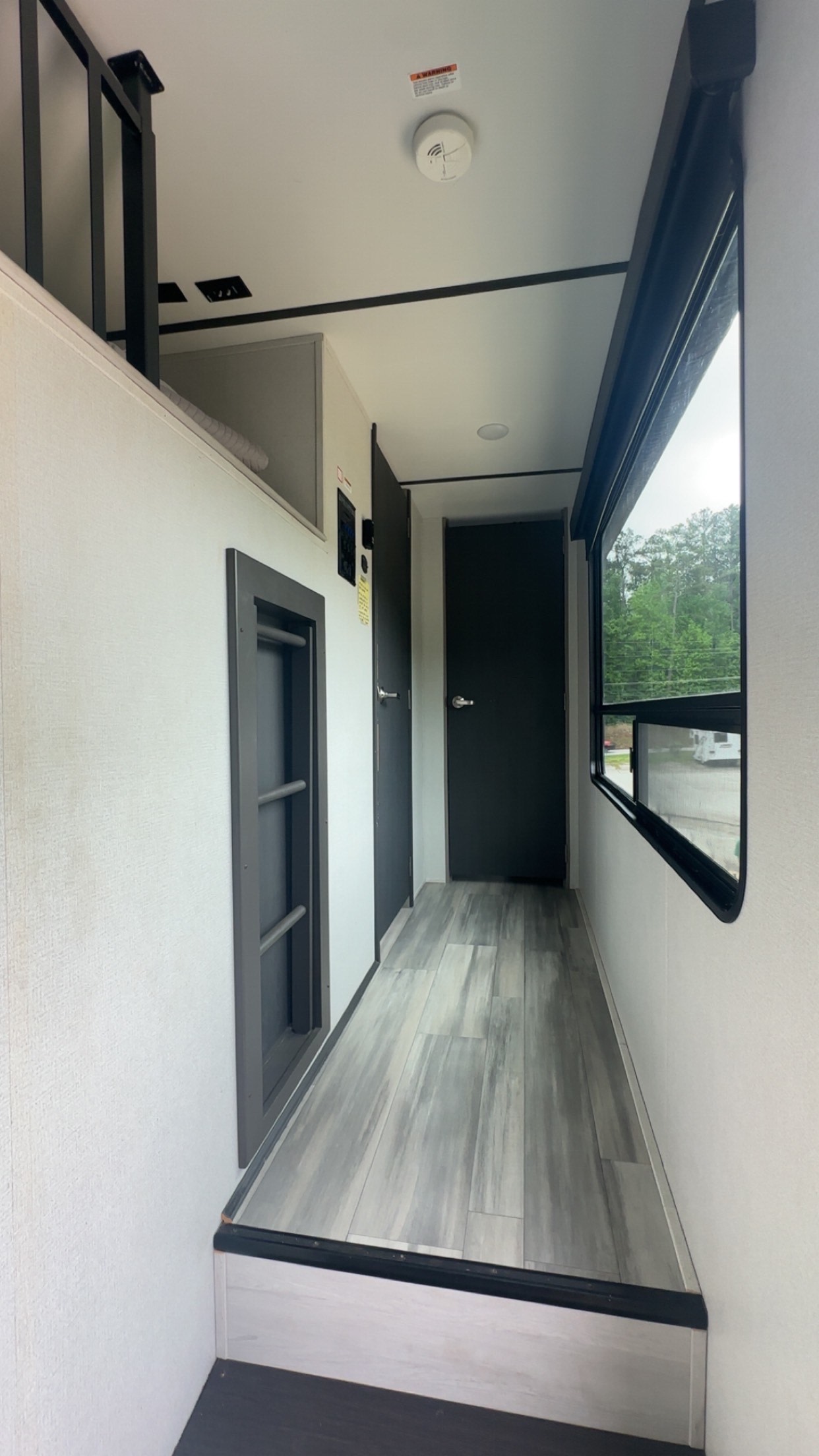 Inside an RV rental, a modern hallway features wood-look flooring, a loft with railing, built-in ladder, and large window.. Keystone Sprinter 2022