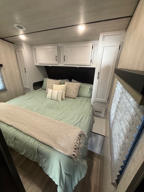 Cozy RV rental bedroom: light green bed, ample overhead/side storage, and a bright window with blinds. Perfect for travels.. Genesis Supreme Rv Genesis Supreme 2025