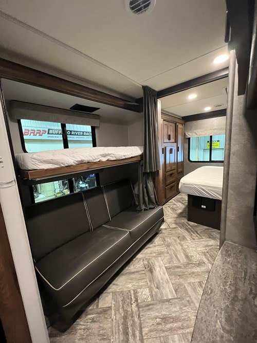 RV rental interior showing a bunk bed over a sofa, a cabinet, and a main bed area with wood-look flooring.. SunSeeker 3250LE 2023