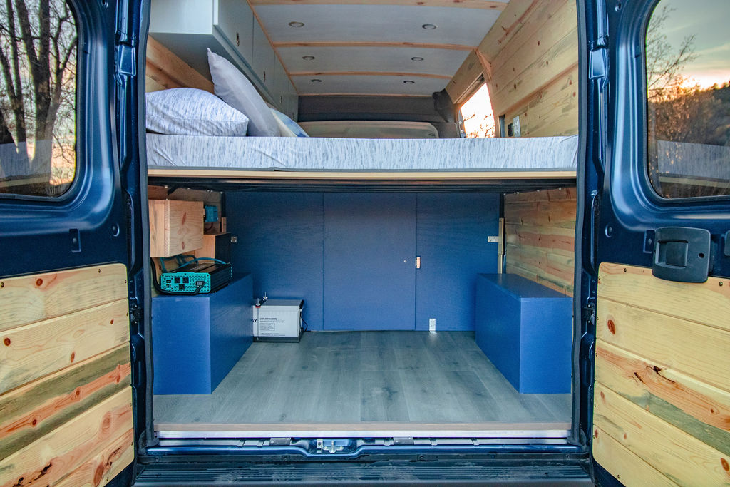 Inside this custom rv rental campervan, see the raised bed, blue storage, and wood accents.. Dodge Ram Promaster 1500 2020