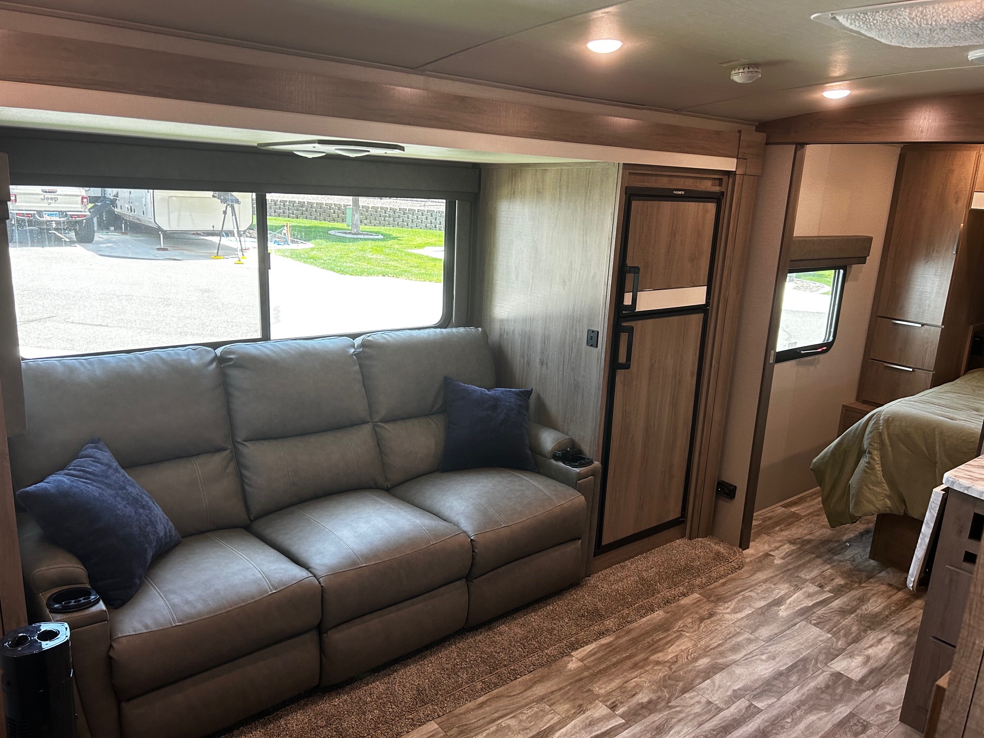 Inside a modern RV rental: comfortable living area with recliner sofa, refrigerator, and accessible private bedroom.. Grand Design Imagine 2022