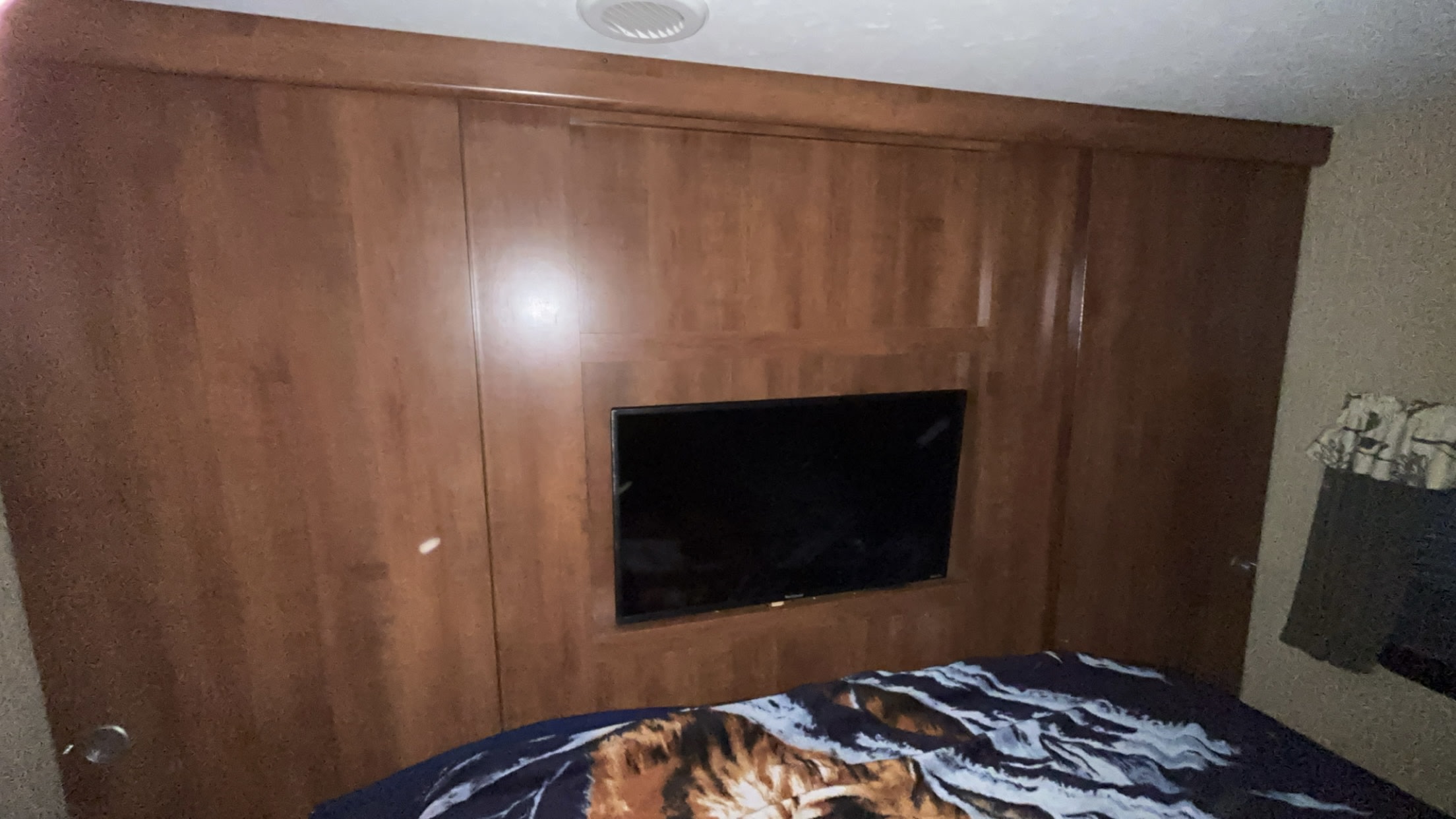 RV rental bedroom interior: warm wood paneling, wall-mounted TV, and a bed with a patterned comforter.. Keystone RV Passport Grand Touring 2017