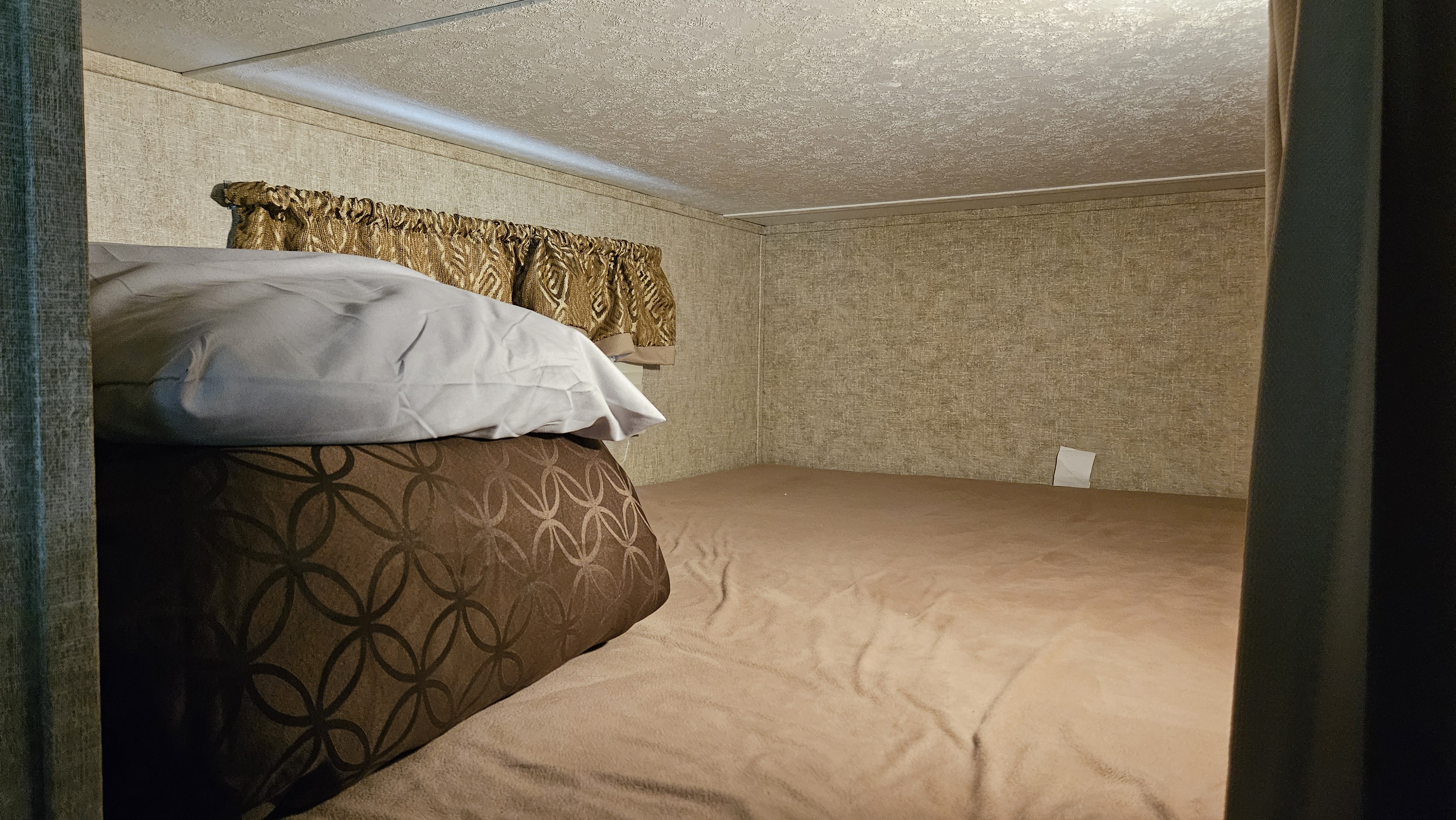 Cozy RV rental bunk area with soft tan bedding, patterned pillows, textured walls, and small decorative curtains.. Forest River Tracer Air 2017