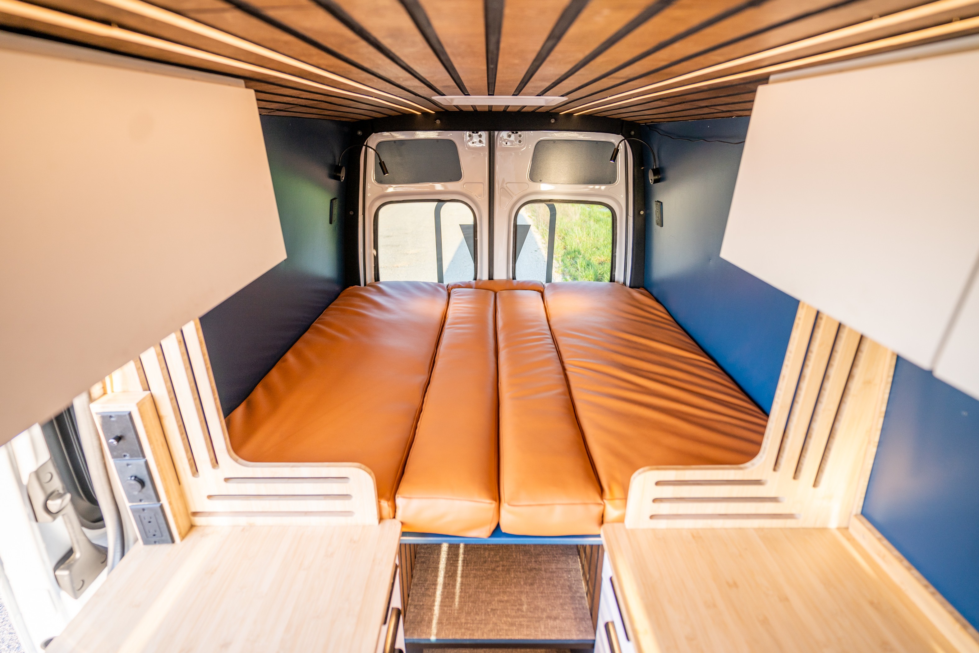 Inside a custom rv rental van: a warm, inviting interior with a brown bed, wood ceiling, and blue walls.. Mercedes-Benz Sprinter 2024