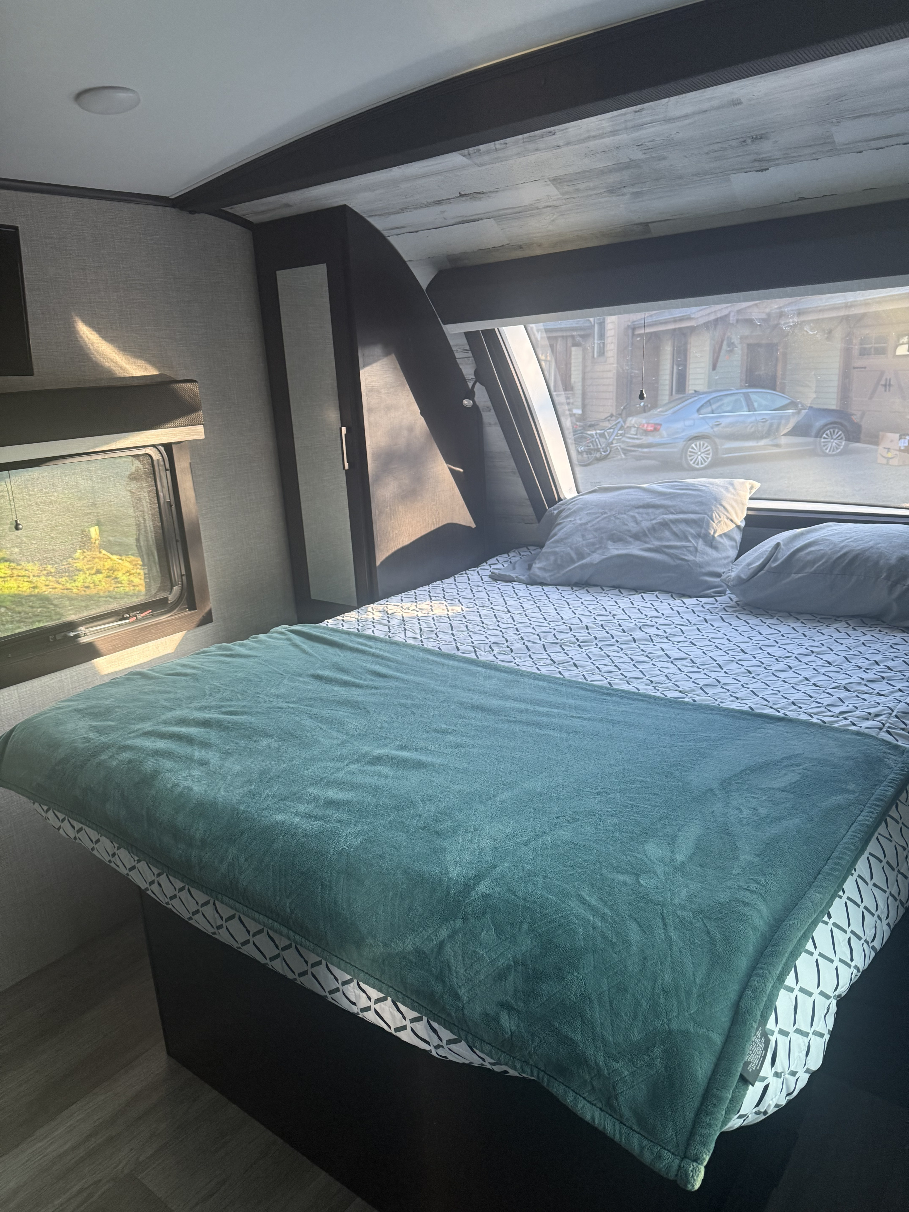 Bright RV rental bedroom showcasing a comfy bed with teal blanket and expansive windows revealing an outdoor scene.. Jayco White Hawk 2023