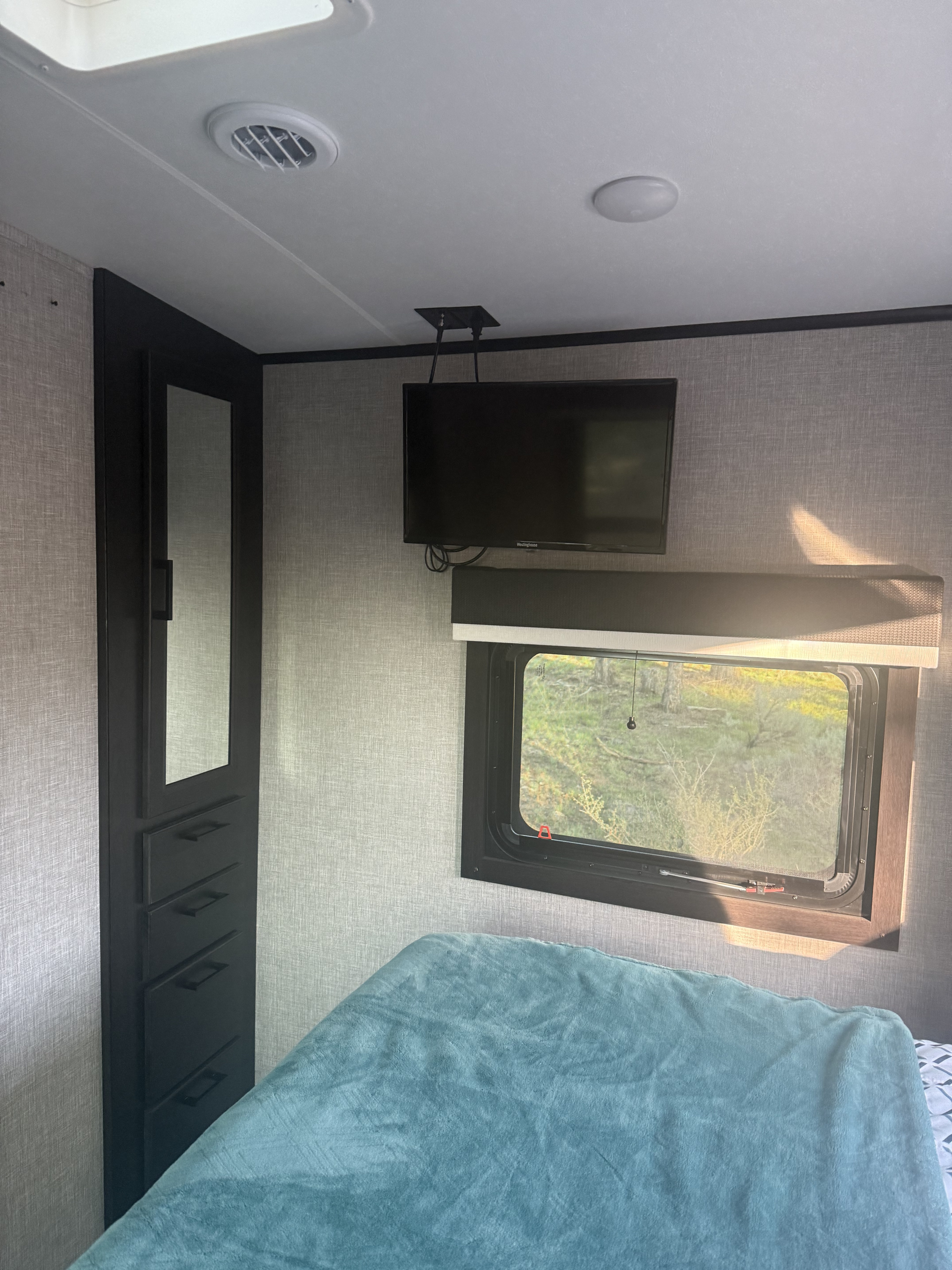 Cozy RV rental bedroom featuring a comfy bed, window view, ceiling-mounted TV, and built-in storage.. Jayco White Hawk 2023