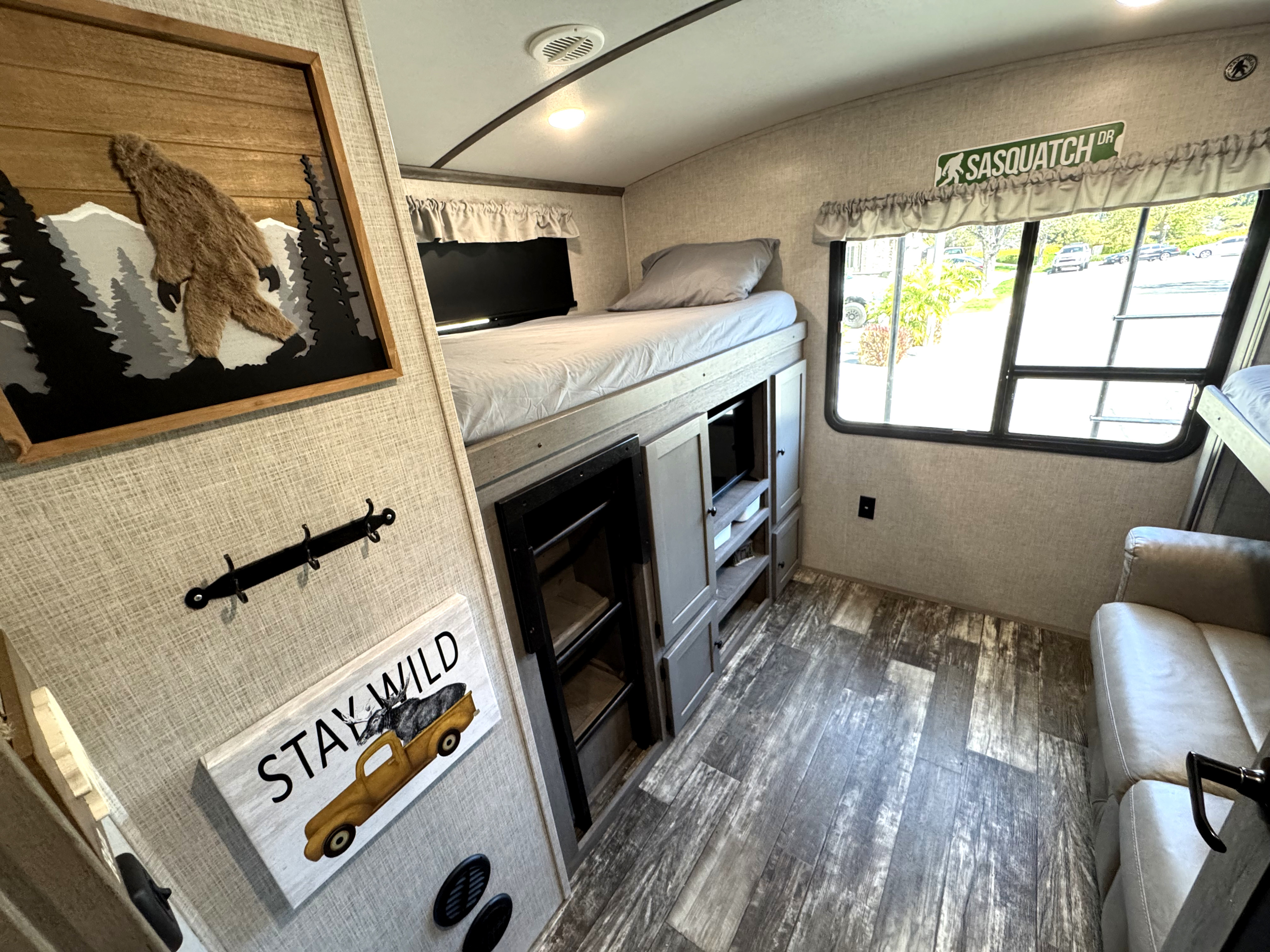 Cozy RV rental interior showing a bunk bed, sofa, wood floor, and Sasquatch-themed wall decor for an adventurous stay.. Keystone RV Outback 2020