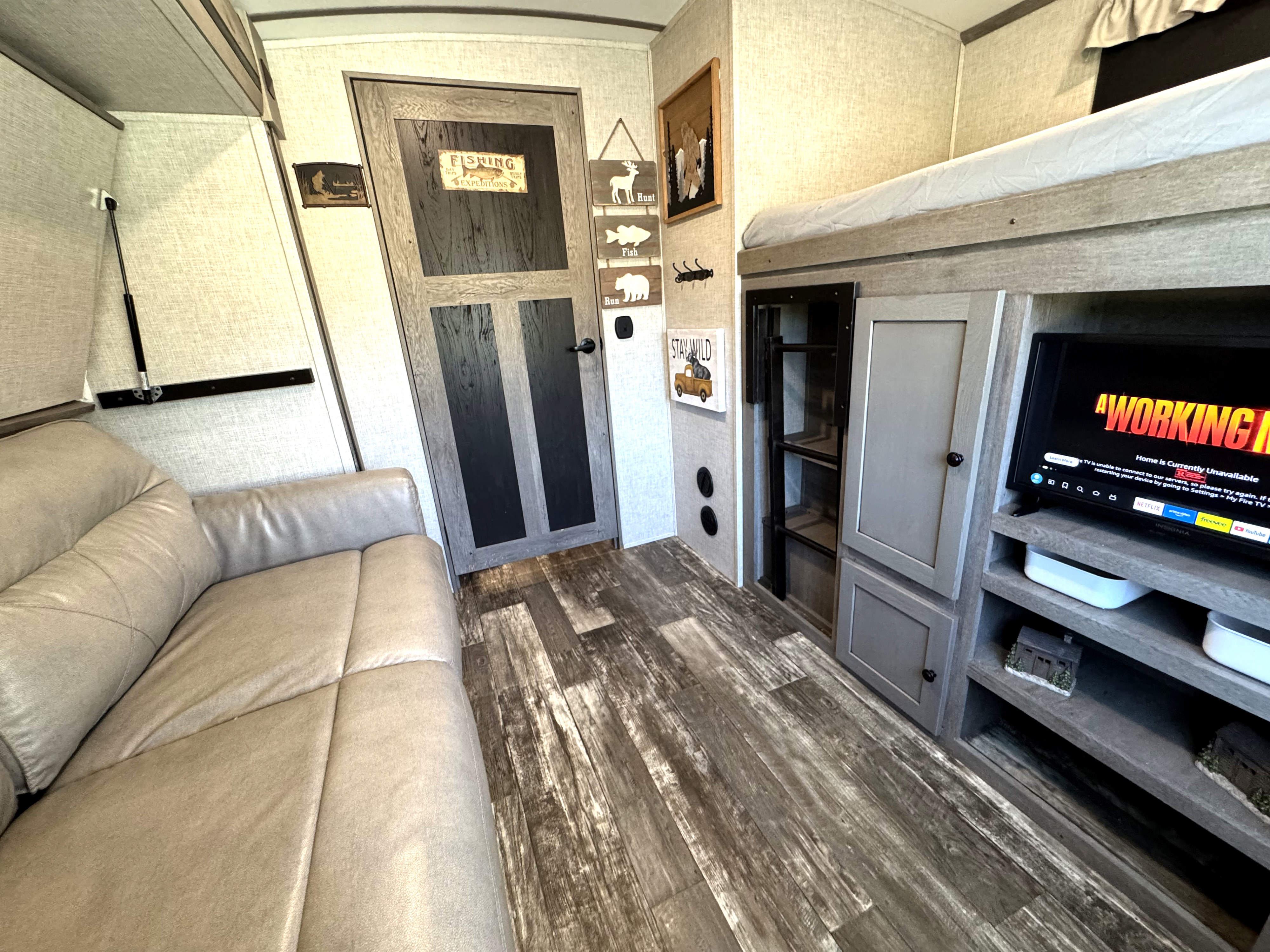 An RV rental's cozy interior with a tan couch, wood-look floor, bunk beds, and a TV showing a service error.. Keystone RV Outback 2020