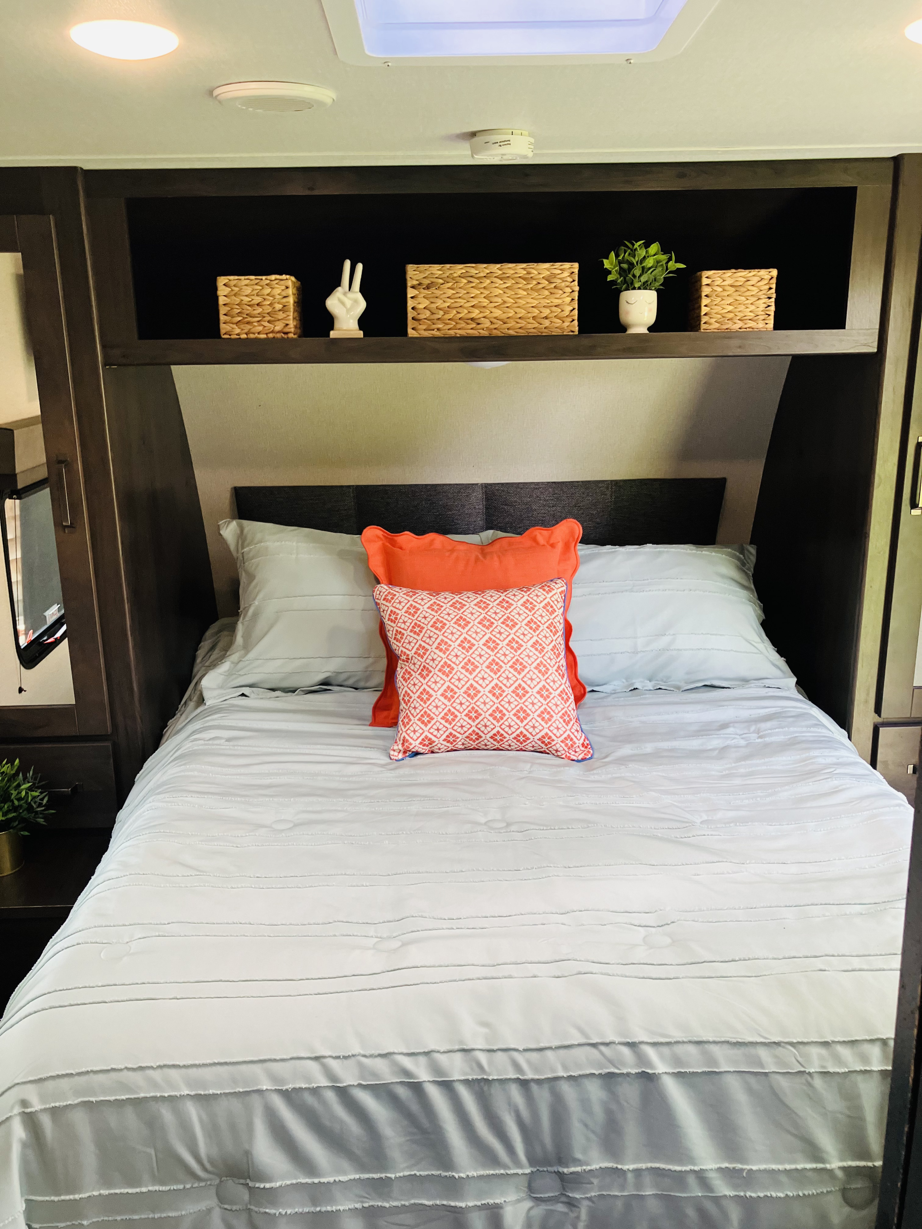 Cozy RV rental bedroom featuring a comfortable bed with light blue bedding, orange decorative pillows, and overhead storage shelves.. Grand Design 265BH 2023