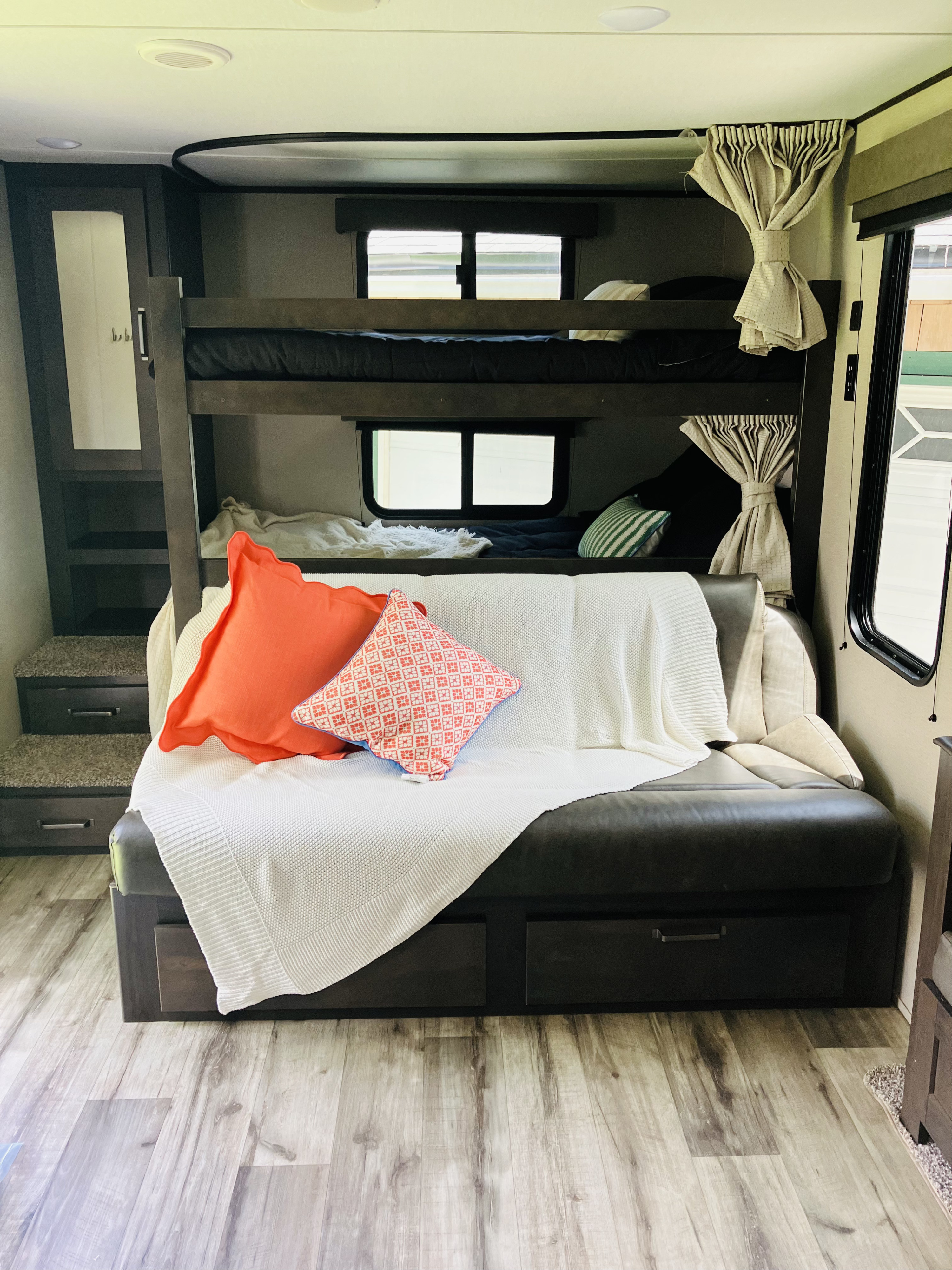Comfortable RV rental interior featuring bunk beds, a cozy couch with pillows, and built-in storage steps.. Grand Design 265BH 2023