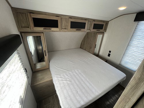 This RV rental bedroom features a large bed, wood-look overhead cabinets, and mirrored closets, creating a functional, compact space.. Alpha Wolf 23DBH 2022