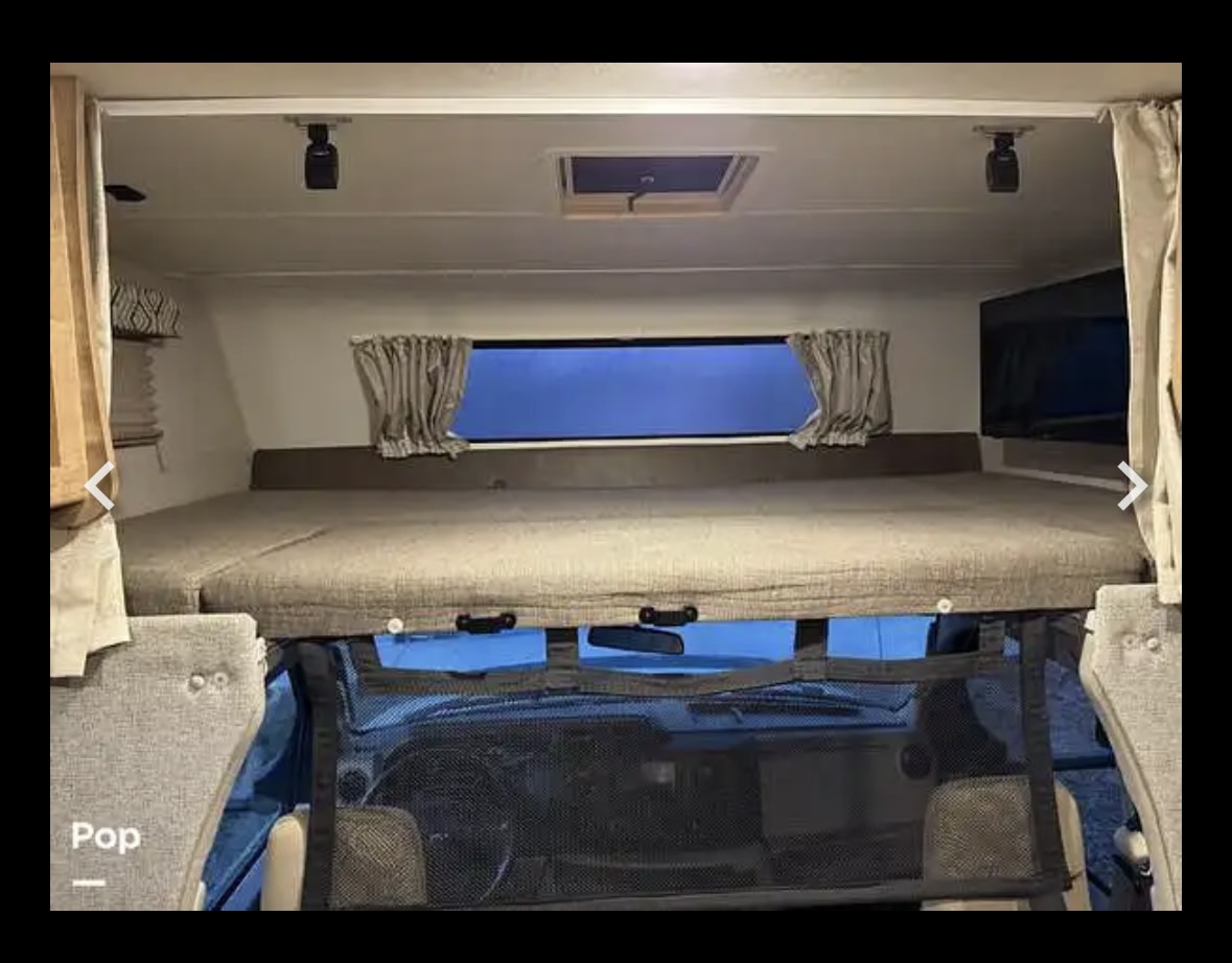 Inside this RV rental: a comfy cab-over bunk with mattress, window, and lights, providing extra sleeping space.. Coachman Leprechaun 2020