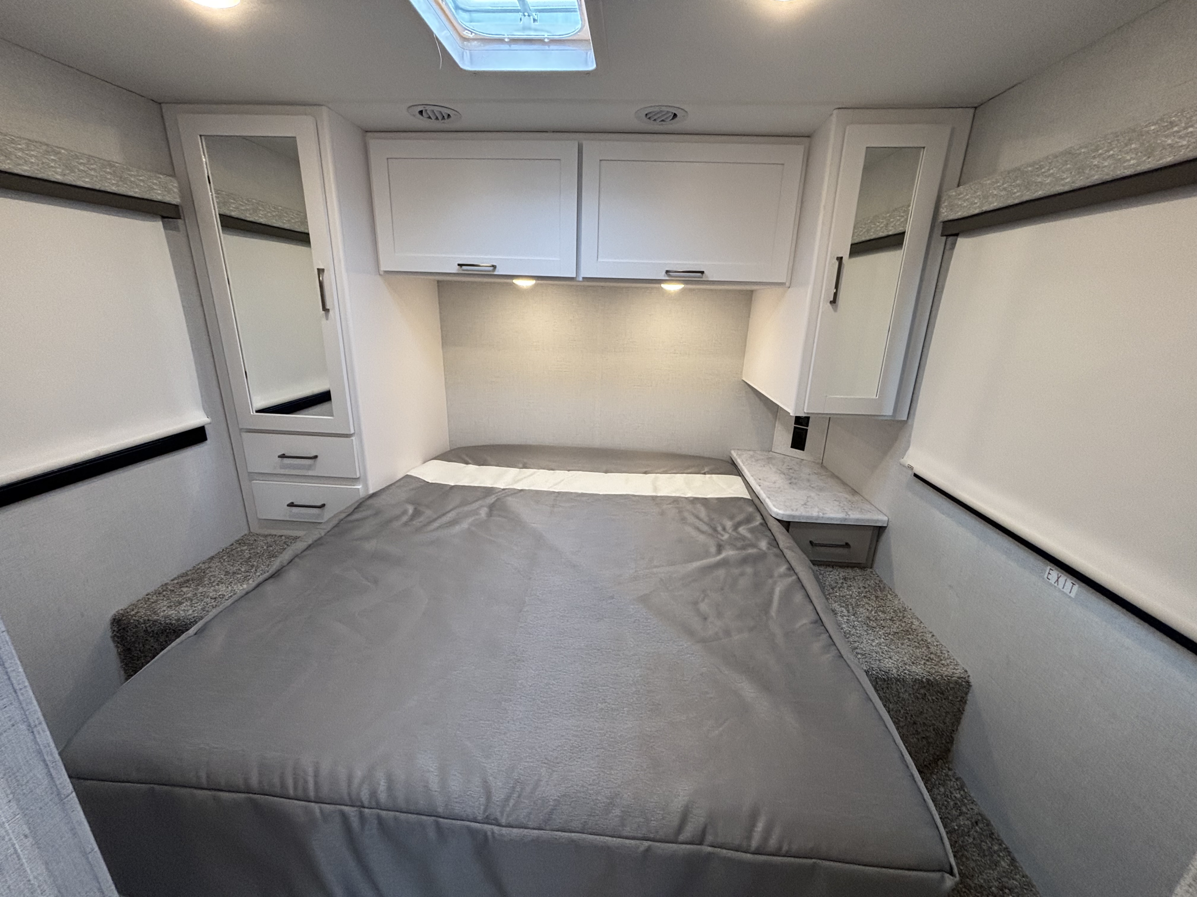 Compact RV rental bedroom with a comfy grey bed, overhead cabinets, skylight, and side storage for travel comfort.. Thor Motor Coach Four Winds 2026