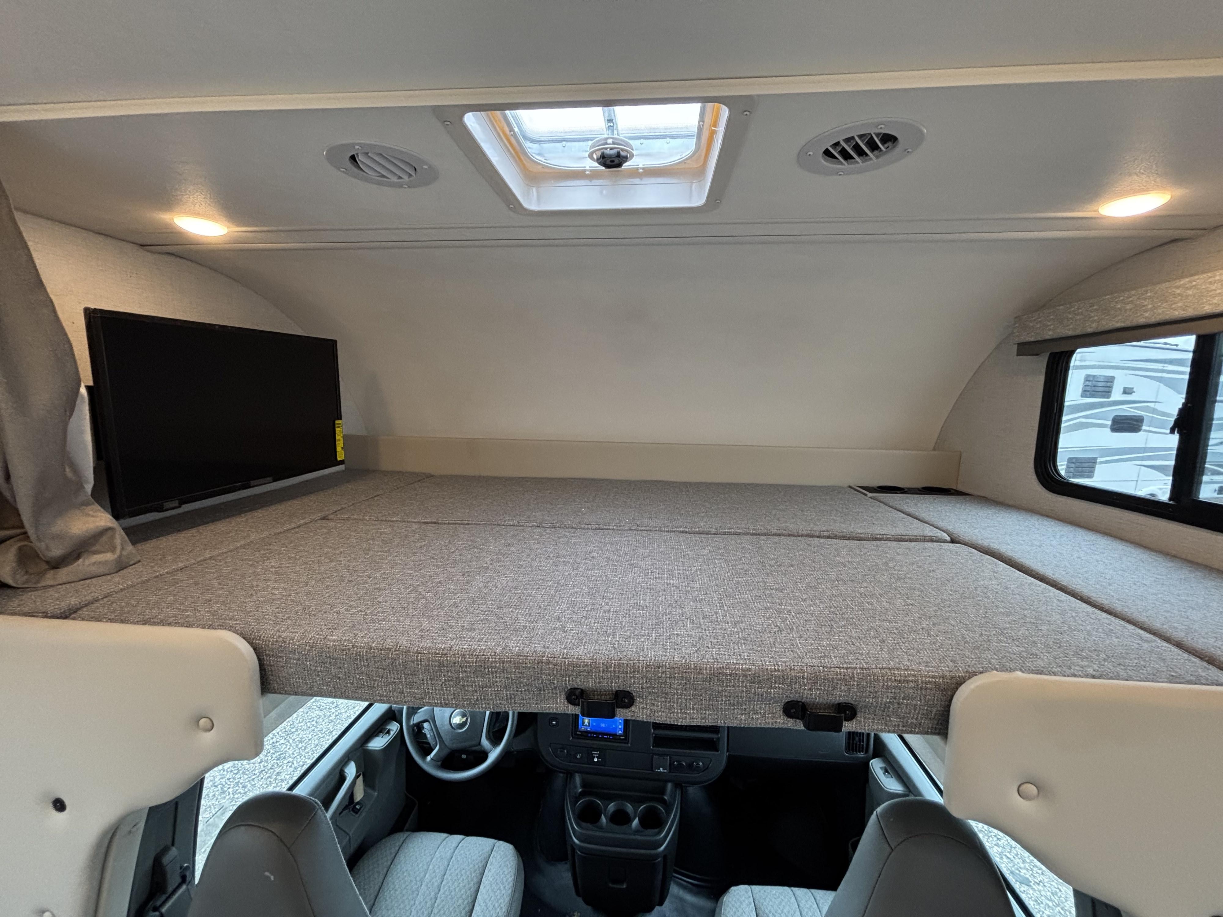 Discover comfort in this RV rental's cab-over bunk area, complete with a TV, skylight, and driver's cockpit view.. Thor Motor Coach Four Winds 2026