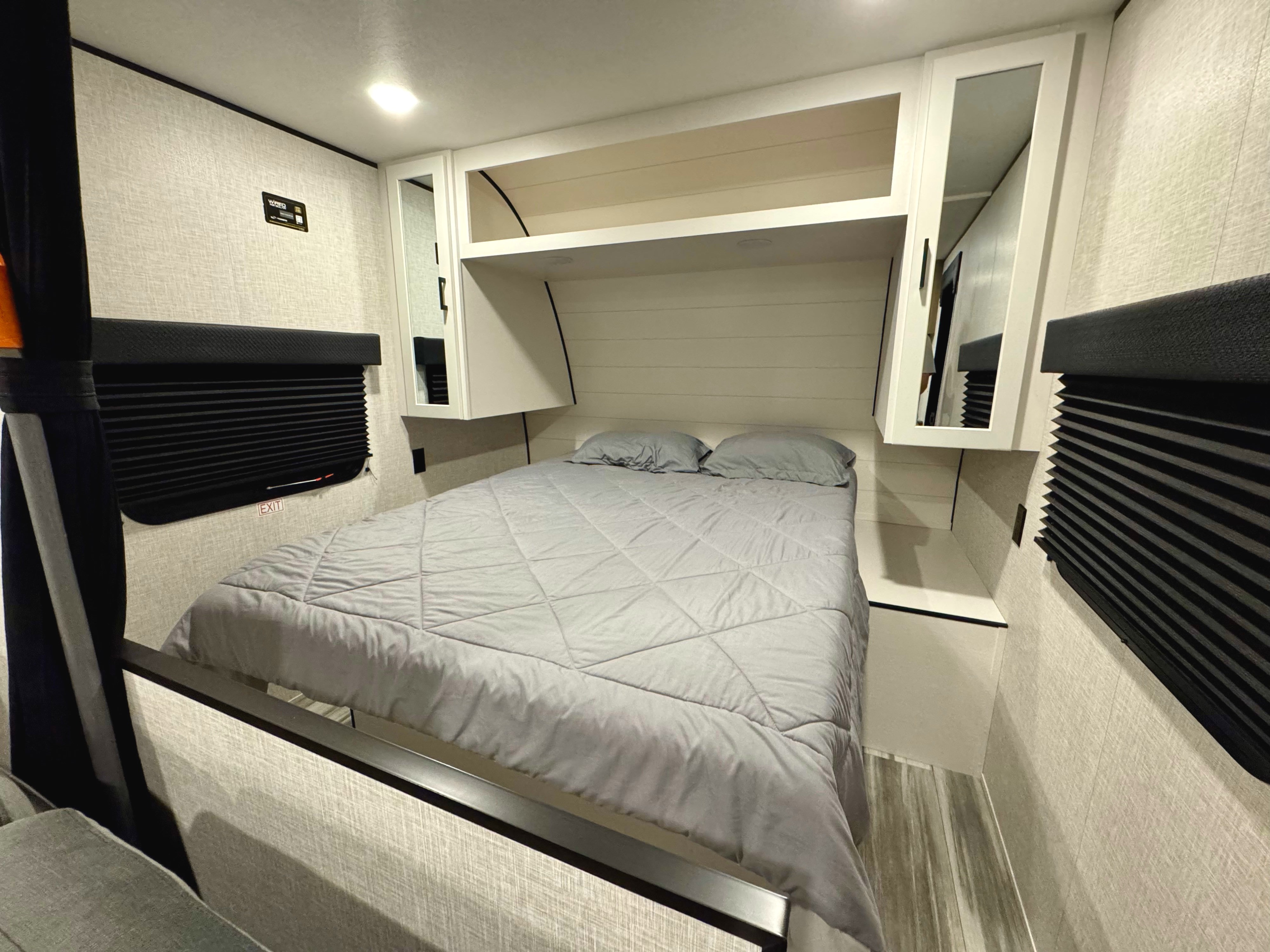 Cozy RV rental bedroom features a comfy bed with gray comforter, overhead storage, and privacy blinds for your travels.. Jayco 260BH 2025
