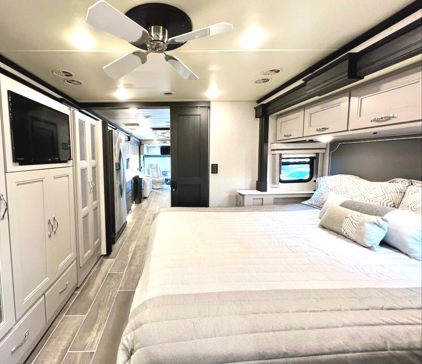 Spacious RV rental bedroom featuring a modern bed, overhead storage, TV, and ceiling fan. A hallway leads to the front.. Thor Motor Coach Venetian 2023