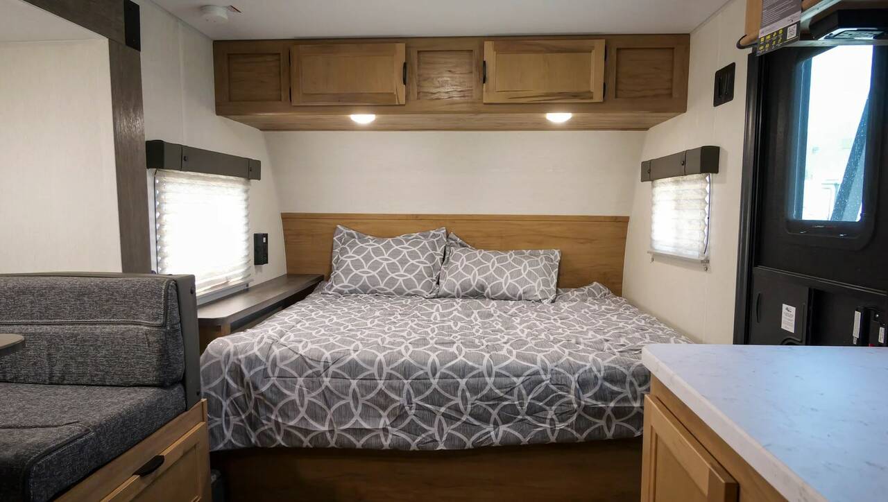 Comfortable RV rental bedroom with gray patterned bedding, overhead storage, side windows, and a dinette.. Cherokee Wolf Pup 2023