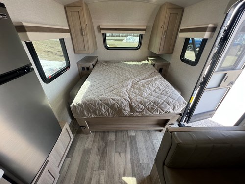 Cozy RV rental interior: features a bed, compact fridge, overhead cabinets, and an open door.. Rockwood GeoPro 2022