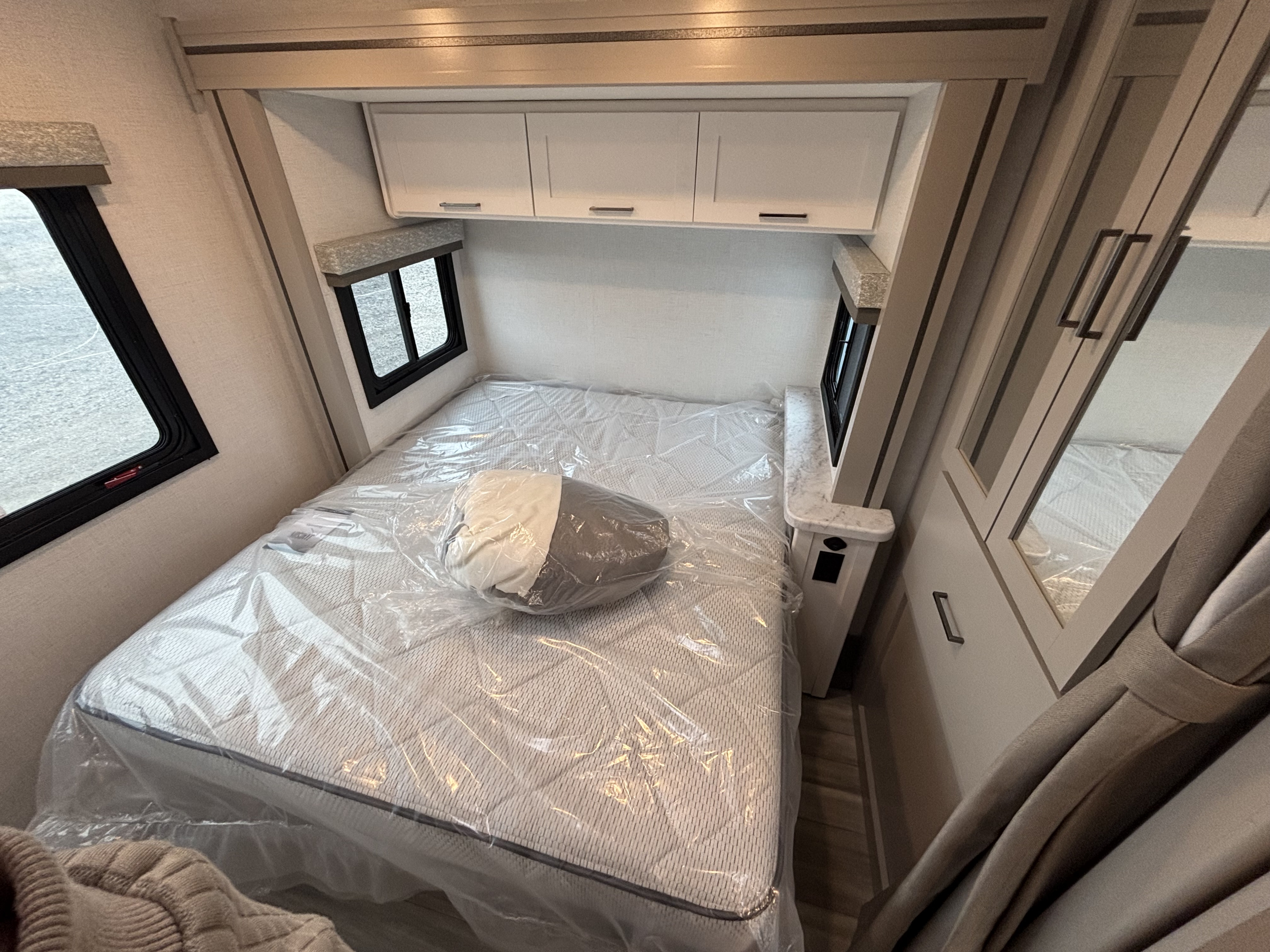 Clean RV rental bedroom featuring a new, plastic-wrapped mattress, overhead cabinets, windows, and built-in storage.. Thor Motor Coach Four Winds 2026
