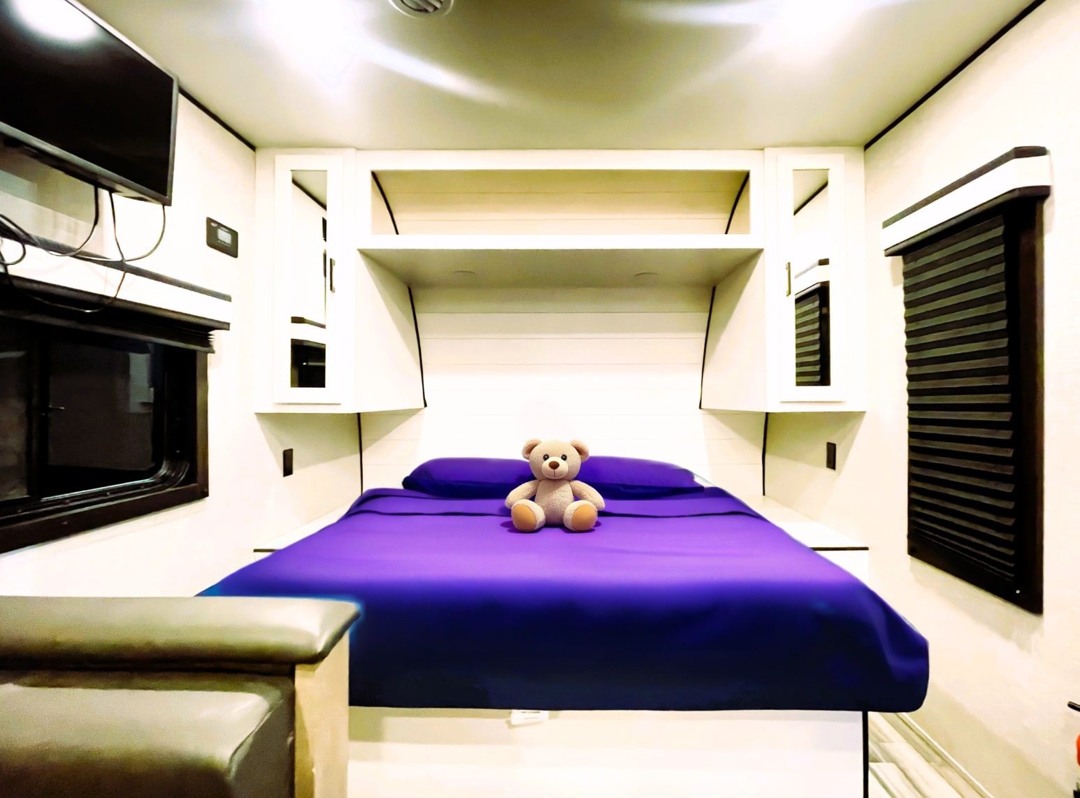 Cozy RV rental bedroom with a purple bed, teddy bear, TV, and storage.. Jayco Jay Feather 2024