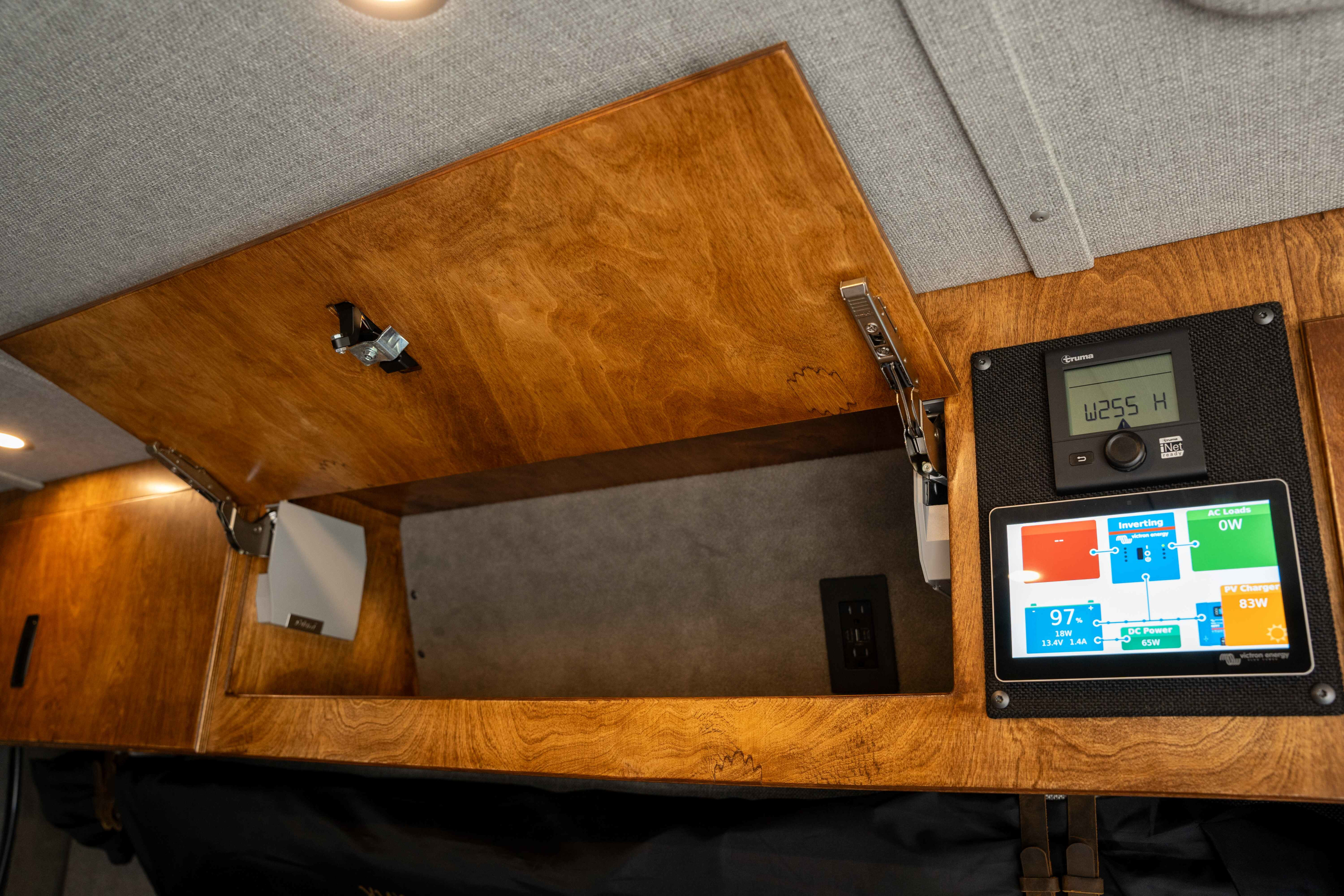 RV rental interior features: an open wooden cabinet and two digital displays for power monitoring and control.. Ford Transit Custom 2022