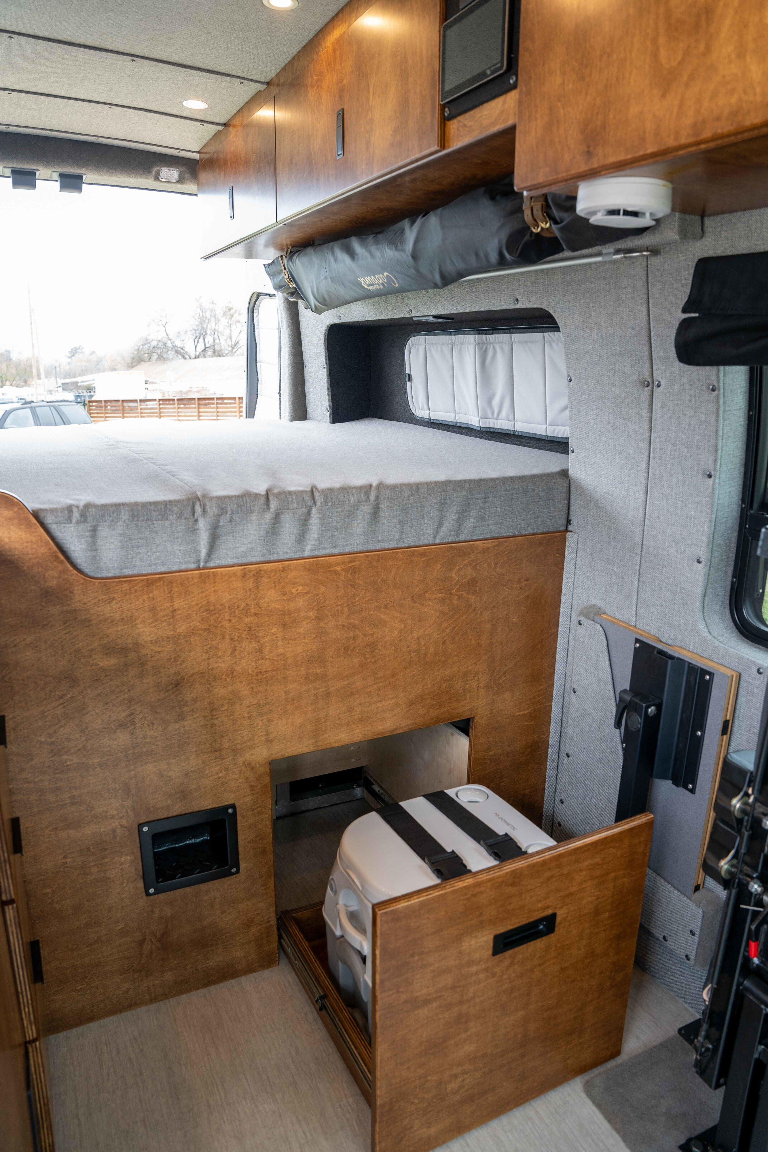 RV rental: Camper van interior reveals a cozy bed, overhead storage, and a pull-out Dometic portable toilet.. Ford Transit Custom 2022