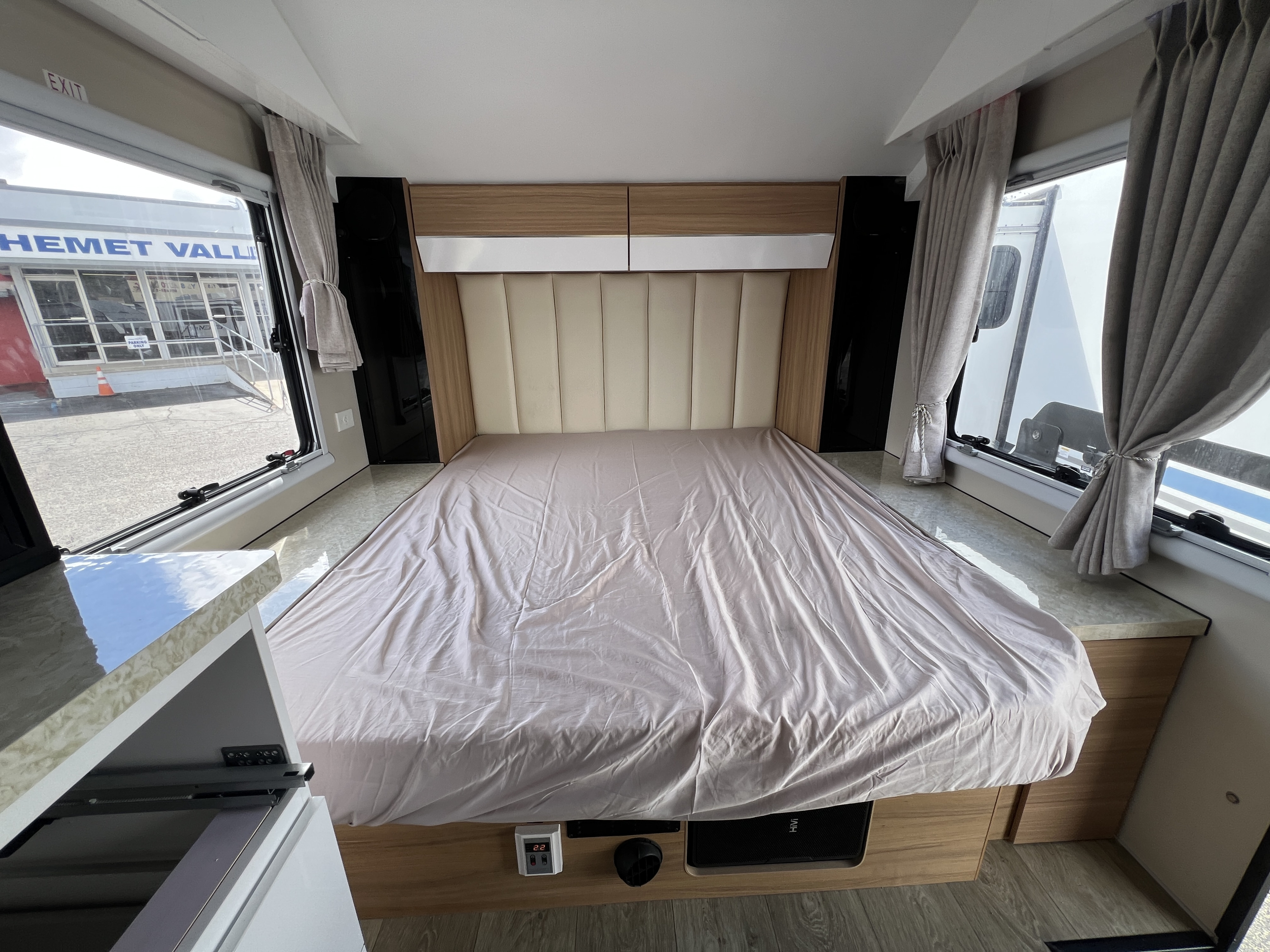 Spacious RV rental bedroom with a comfy bed, overhead cabinets, and windows offering a view of Hemet Valley.. Black Series HQ 19 2025