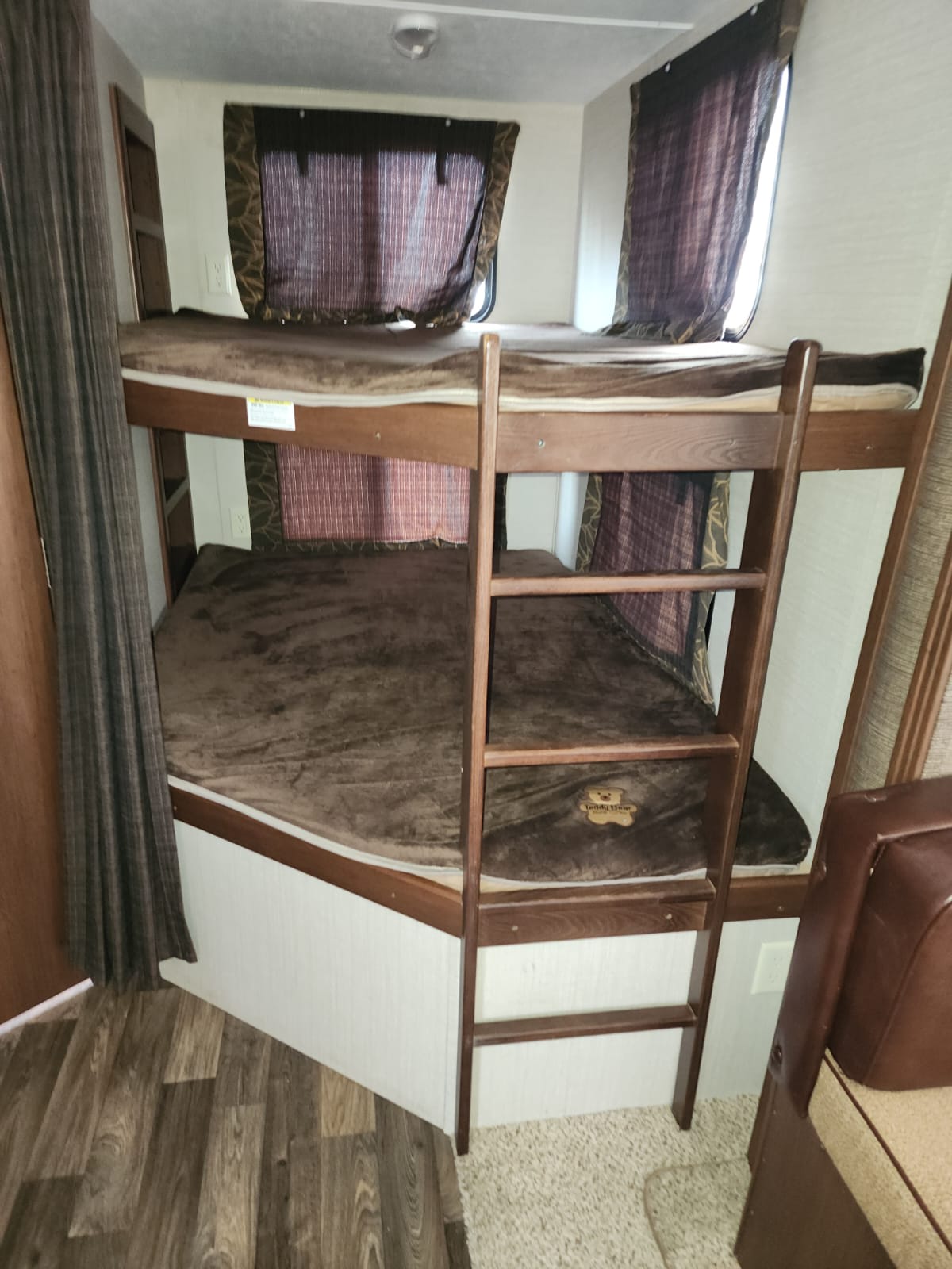 Cozy RV rental sleeping area featuring brown bunk beds with a wooden ladder and windows with curtains. Ideal for family trips.. Keystone RV Bullet Ultra Lite 2015