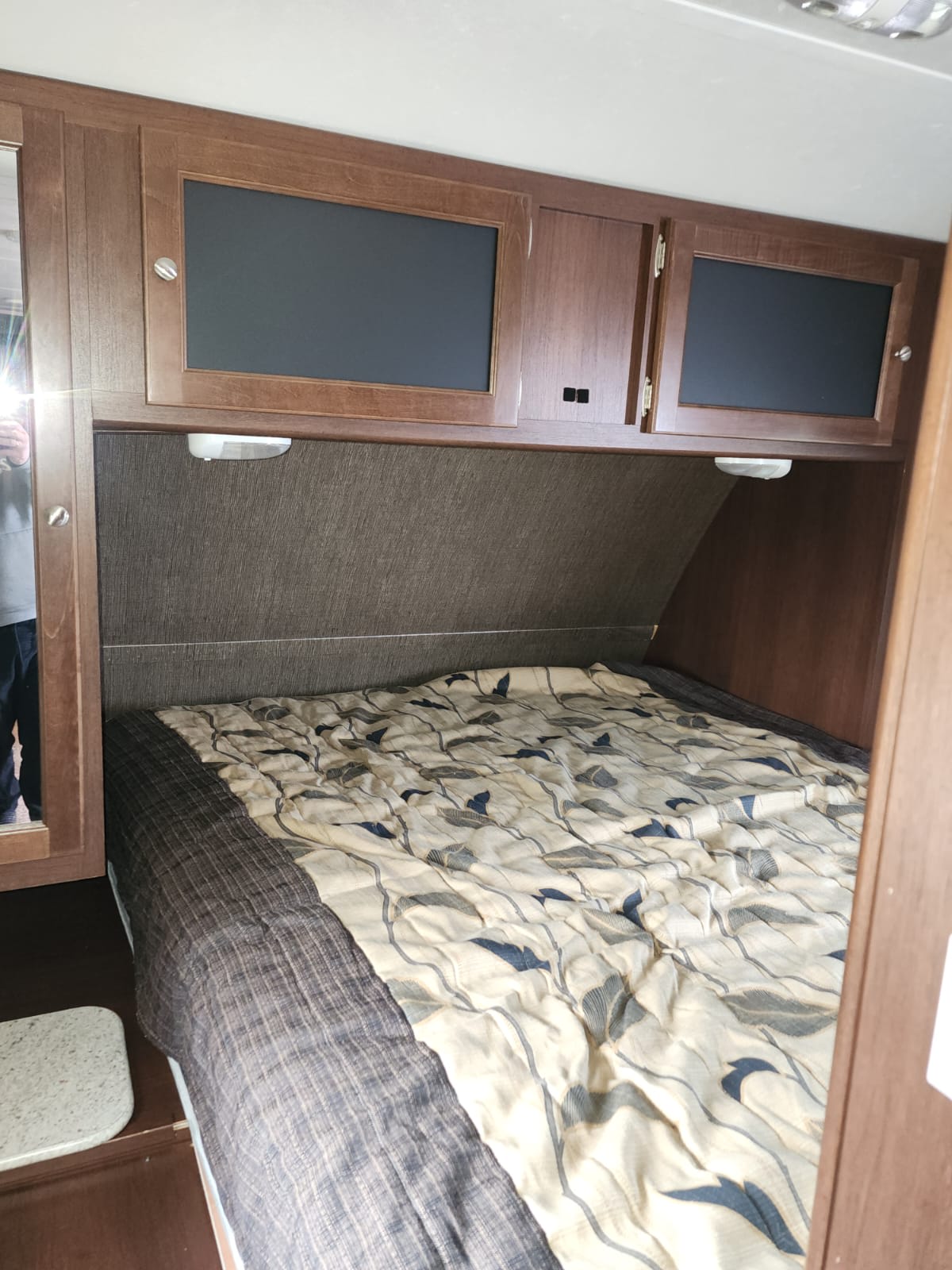 Cozy RV rental bedroom with patterned comforter, wooden overhead cabinets, and reading light.. Keystone RV Bullet Ultra Lite 2015