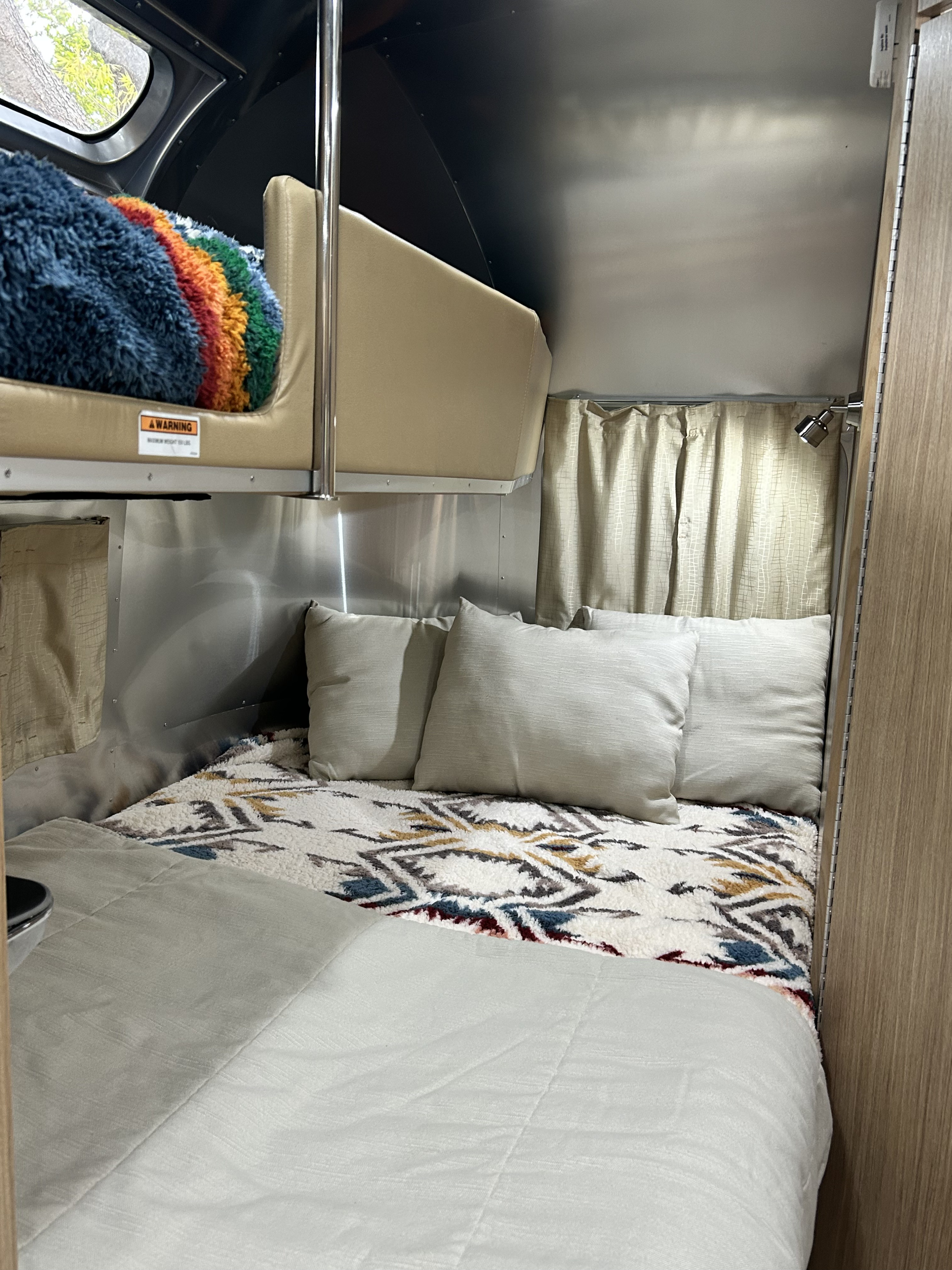 Cozy RV rental interior featuring a main bed with neutral pillows and a colorful blanket on the upper bunk.. Airstream Flying Cloud 2017