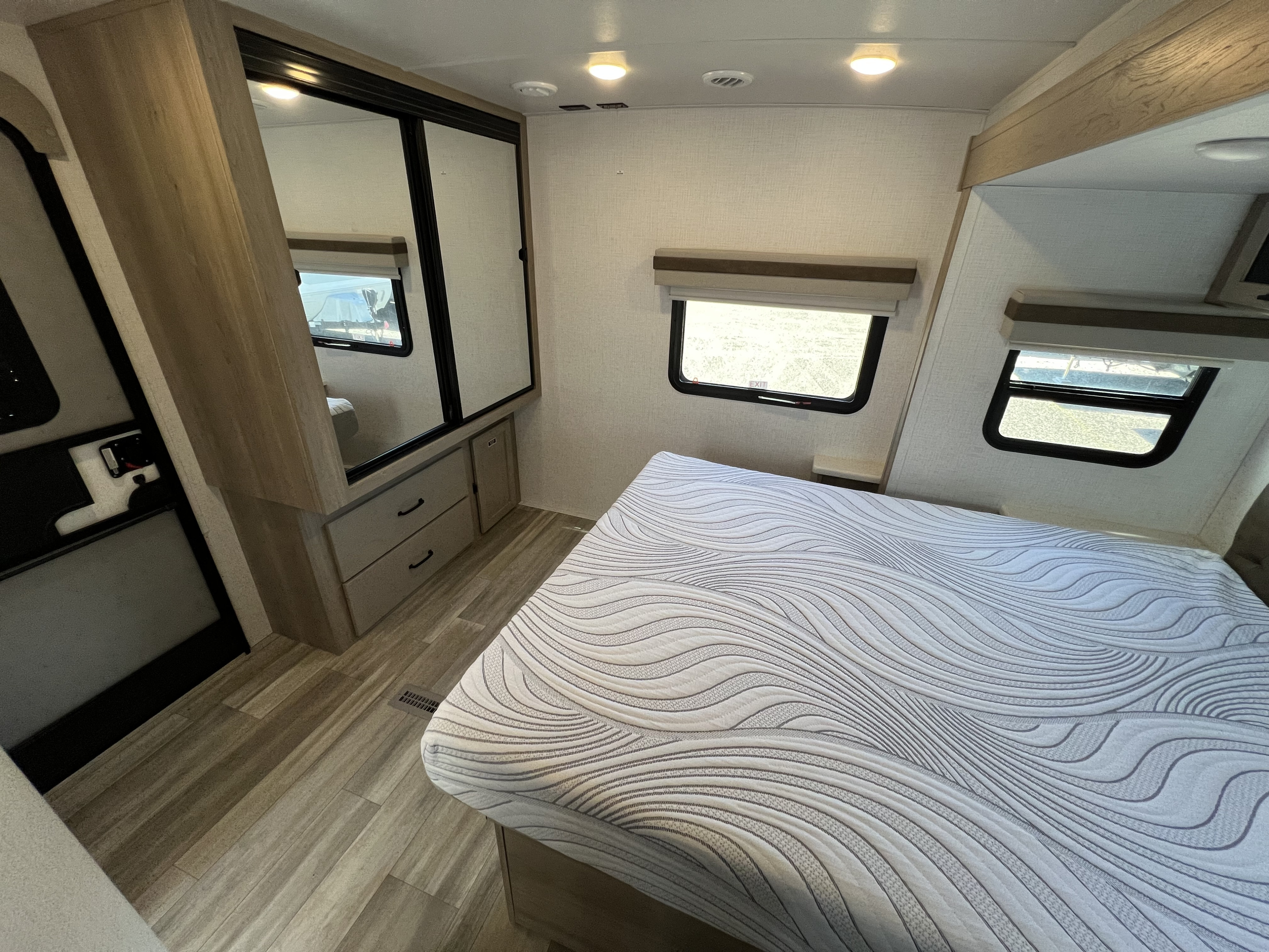 RV rental bedroom with patterned mattress, wood floor, wardrobe, windows, and overhead lighting.. Forest River Rockwood Ultra Lite 2024