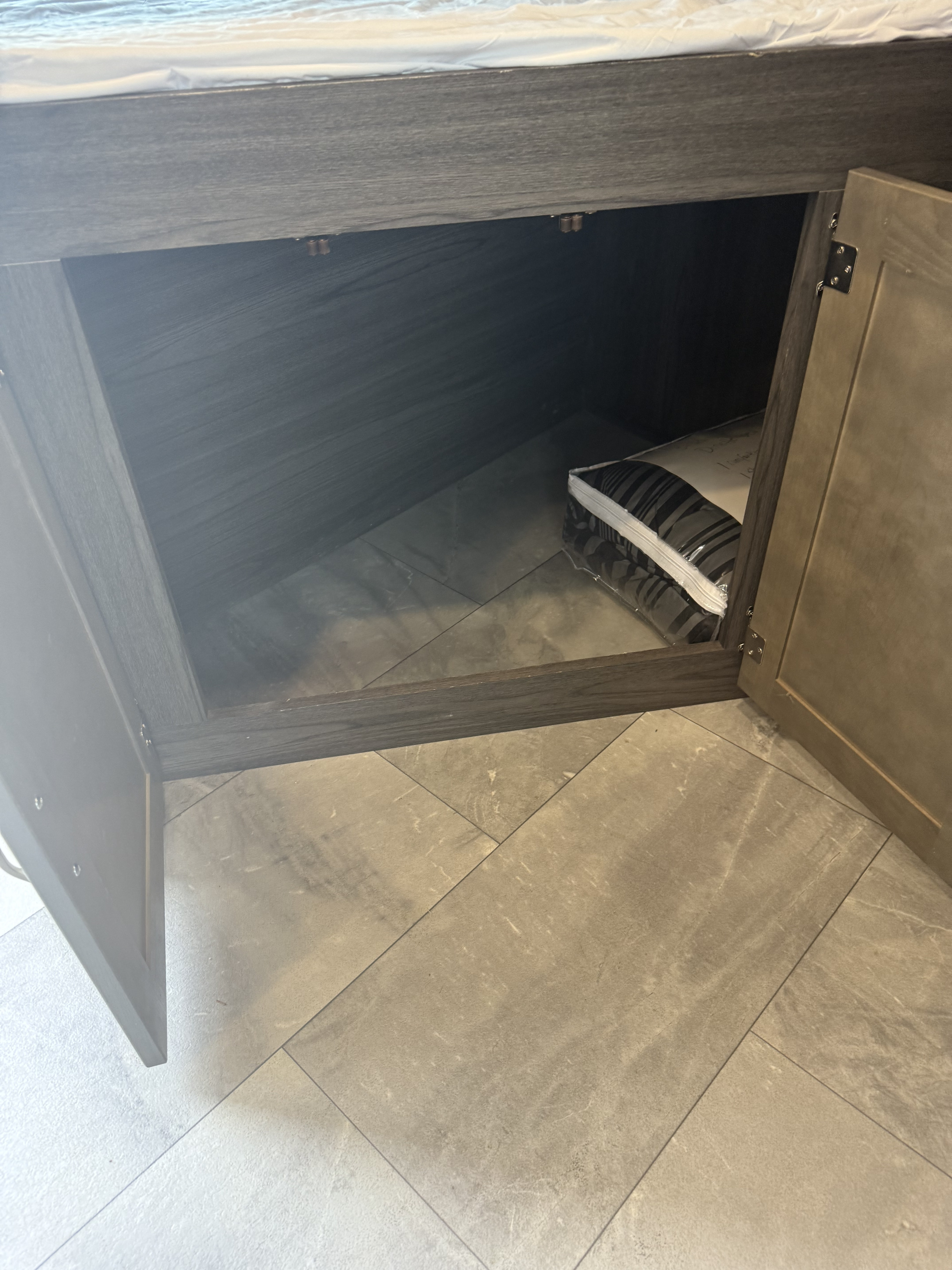 Inside an RV rental's clever under-bed storage, a new, striped bedding set sits on the light gray tiled floor.. Dutchmen Kodiak Ultra Lite 2021