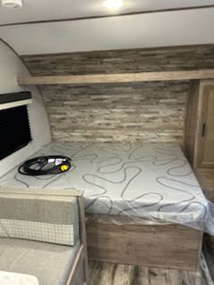 This RV rental bedroom has a new mattress with a swirly pattern, a wood-look headboard, and an overhead shelf. Ideal for travel.. Gulf Stream Ameri-lite 2024