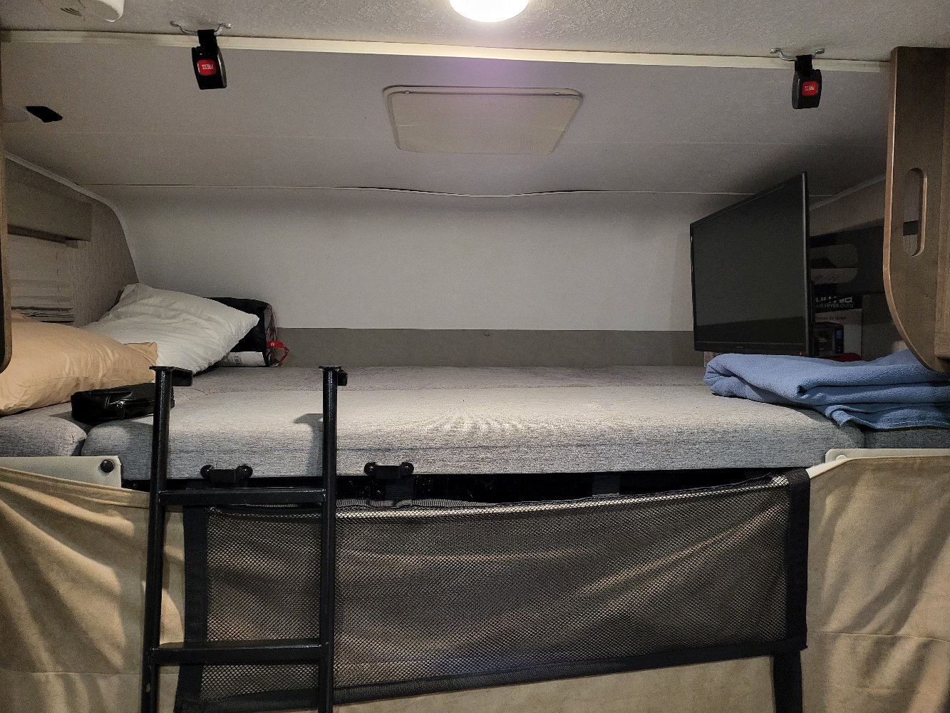 Inside an RV rental: a cozy overhead bunk bed with a ladder, safety net, and TV, ready for travel.. Forest River Coachmen Leprechaun 2022