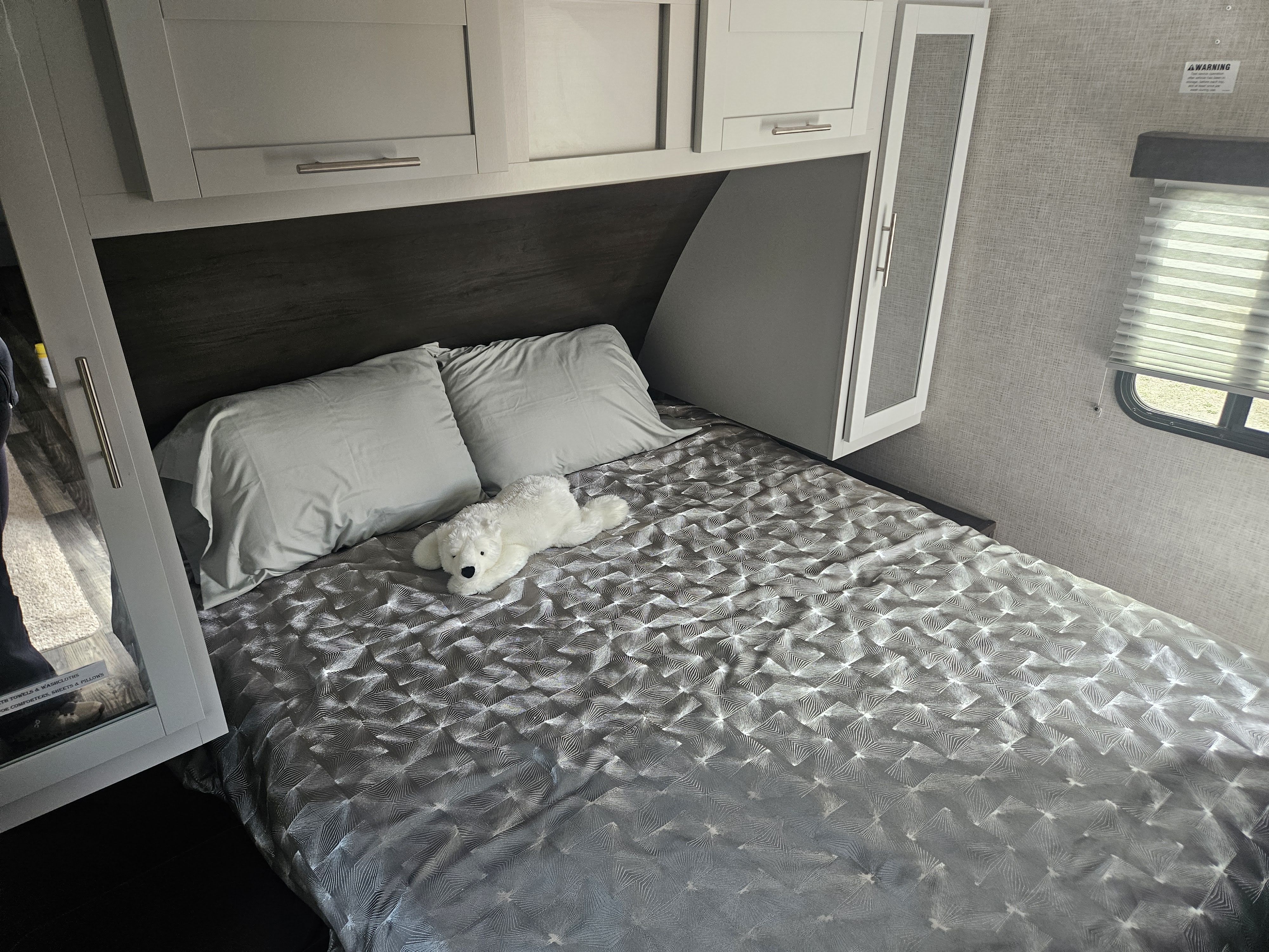 Cozy RV rental bedroom with modern cabinets, soft bedding, and a plush white dog toy. Ideal for a comfortable stay.. Keystone RV Bullet Ultra Lite 2020