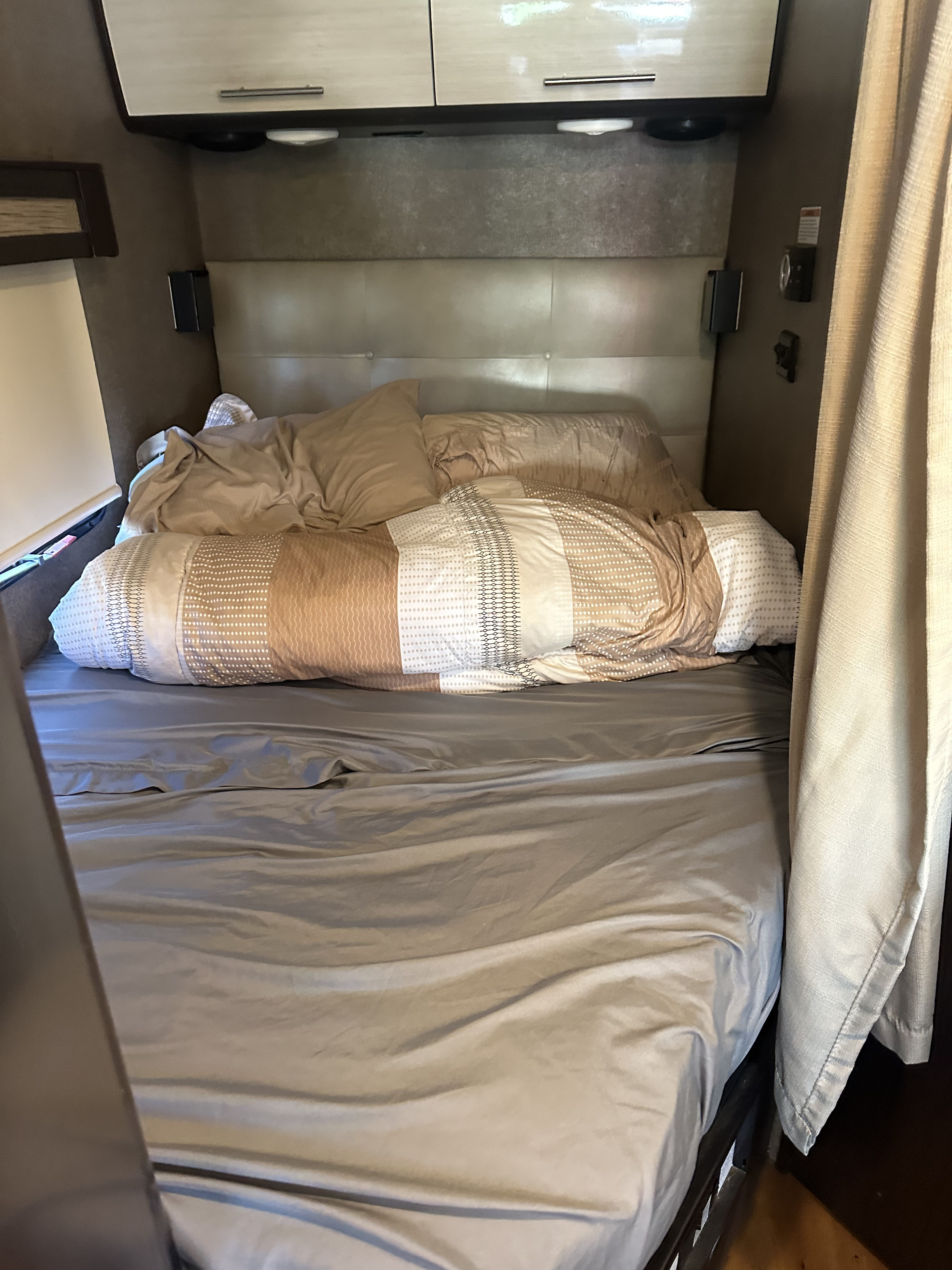 Inside a cozy RV rental bedroom: a comfortable bed with neutral bedding, overhead storage, and wall-mounted lights for reading.. Thor Compass 2017