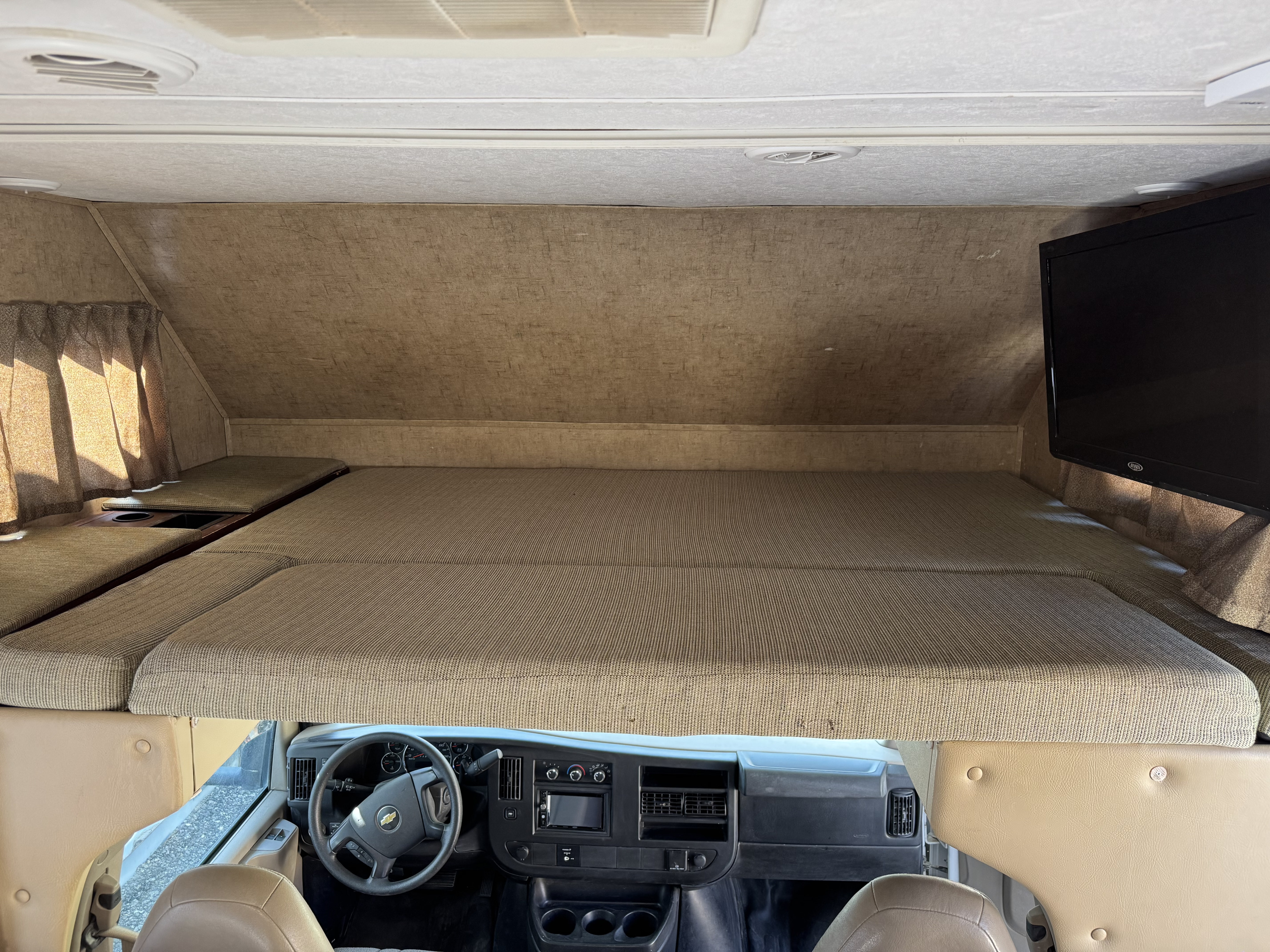 View of an RV rental's cozy cab-over bunk bedroom, featuring comfortable mattress, TV, and the vehicle's cockpit.. Forester LE 2016