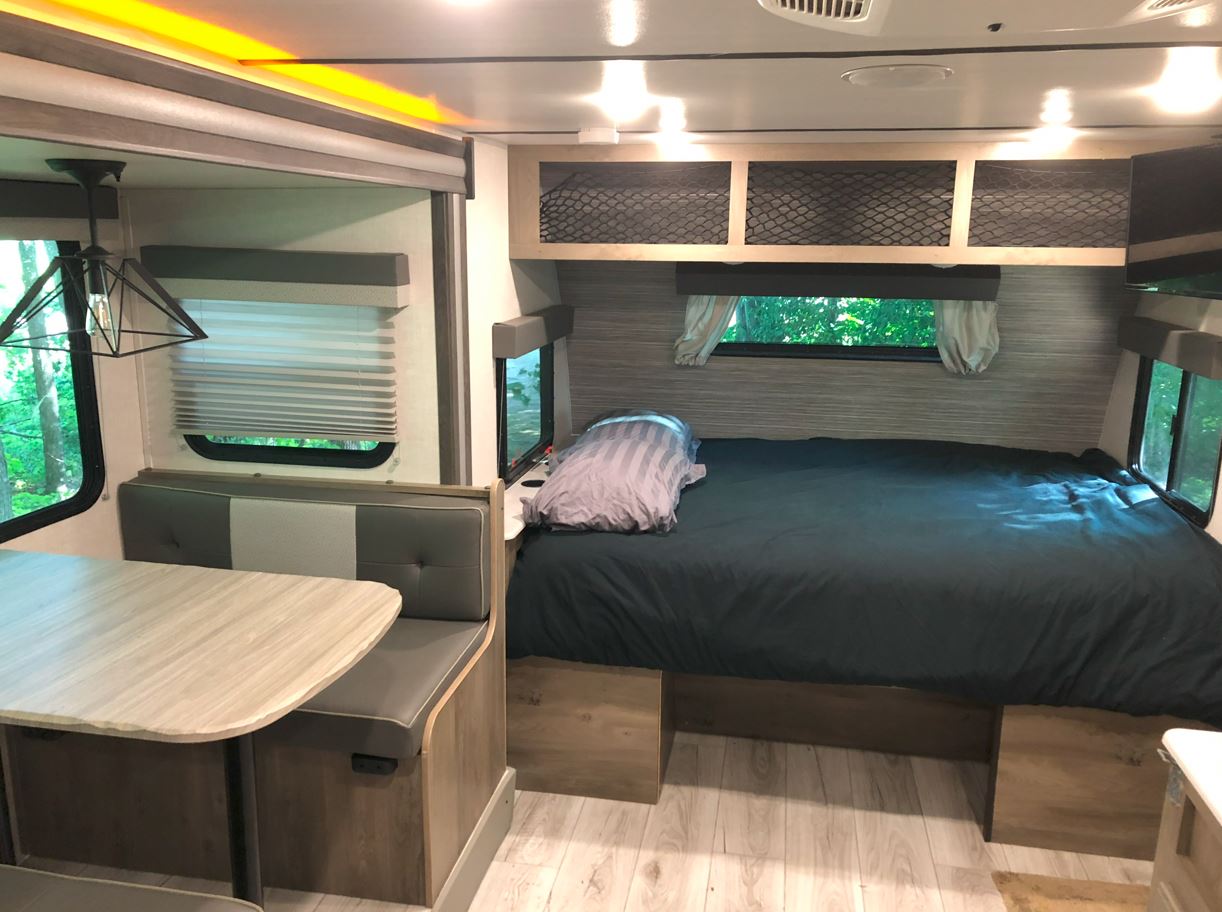 Spacious RV rental interior featuring a cozy dining booth and a full-size bed with windows.. Forest River Surveyor Legend 2021