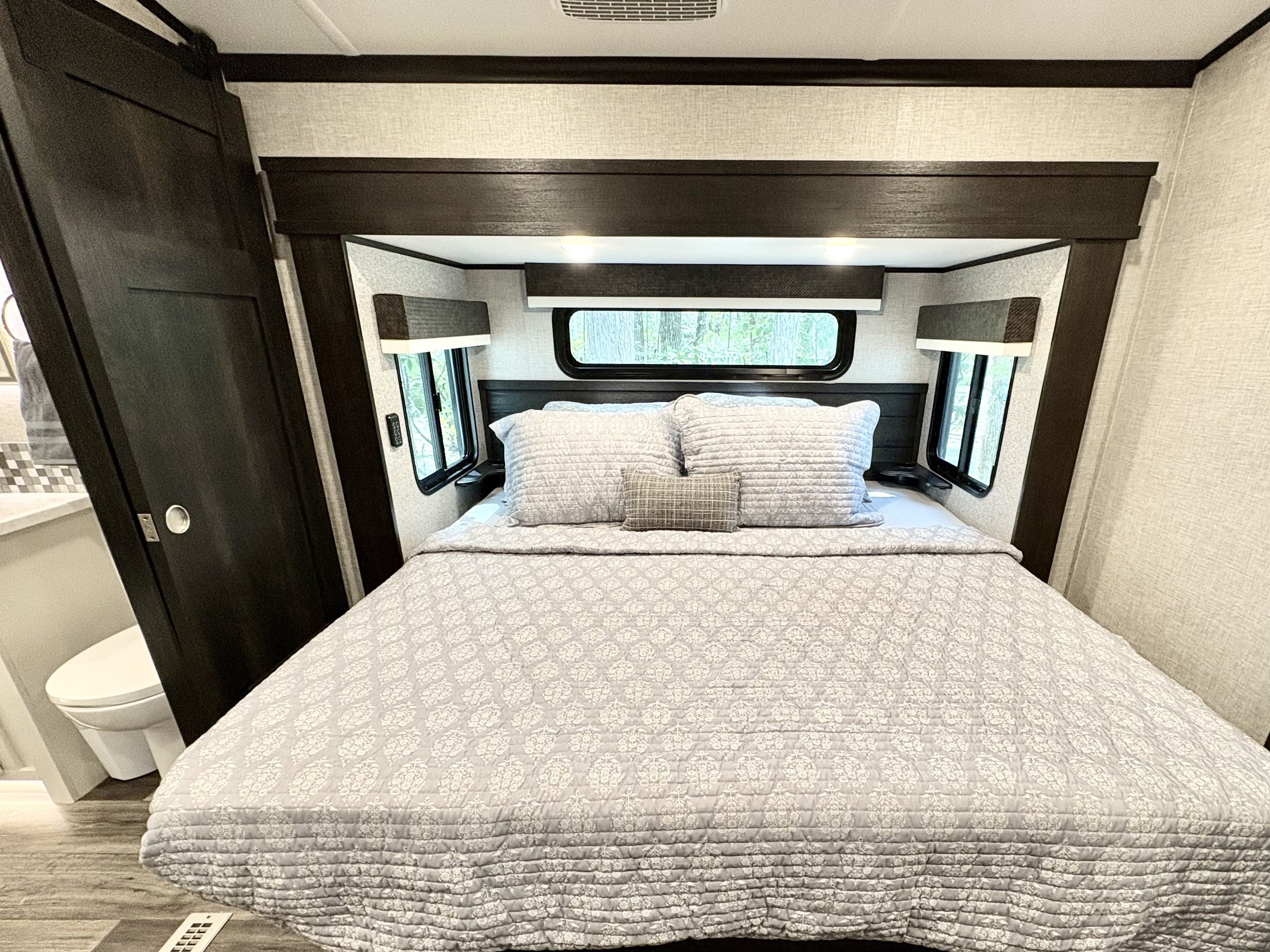 Cozy RV rental bedroom with a queen bed, overhead storage, and windows. Bathroom seen left.. Jayco North Point 2022
