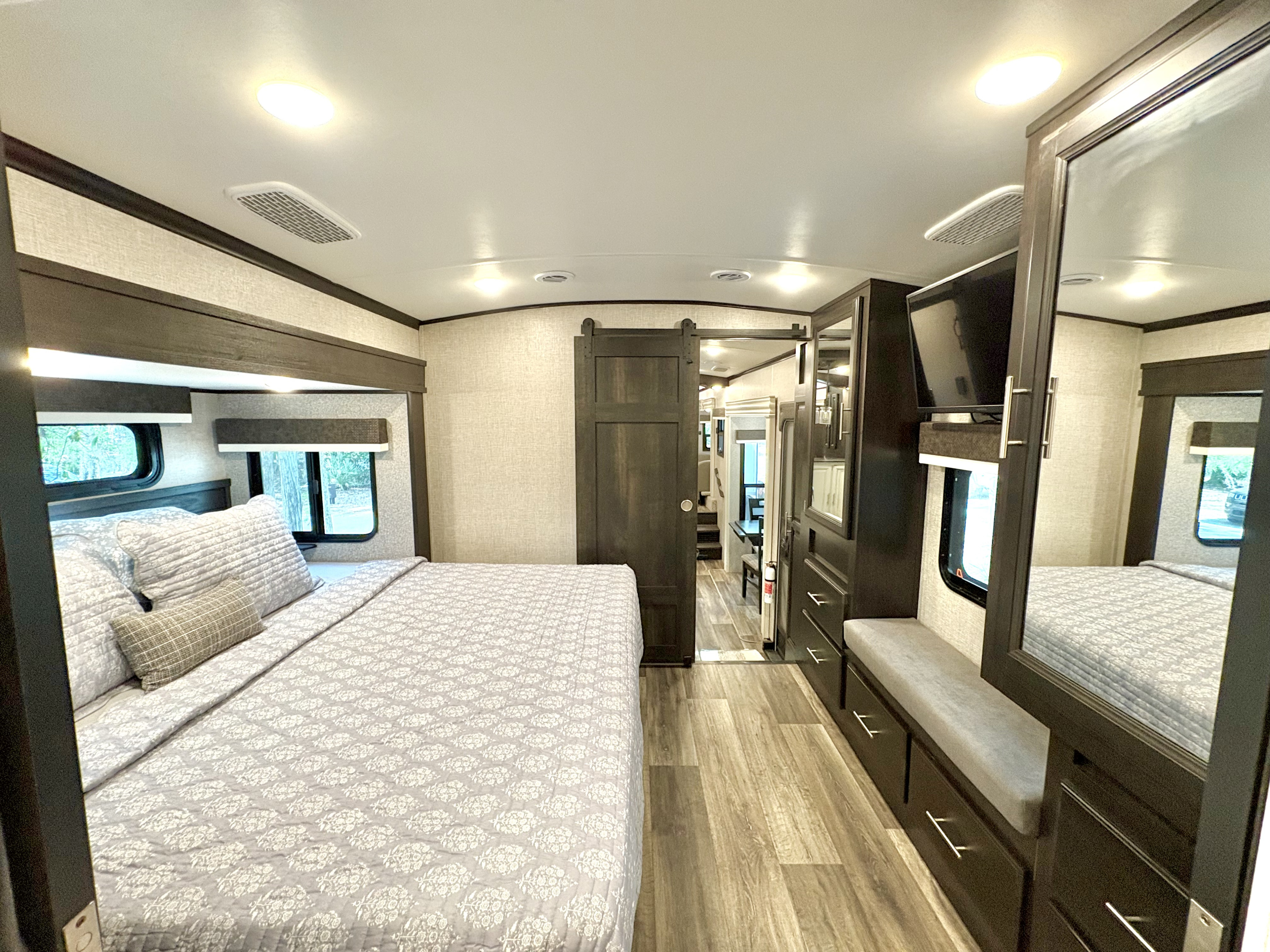 Spacious, modern RV rental bedroom featuring a large bed with light bedding, built-in storage, and a TV. Ready for adventure.. Jayco North Point 2022