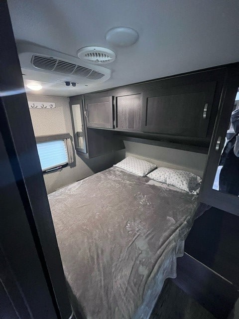 Inside an RV rental bedroom: a neatly made bed, overhead air conditioning, and dark wood cabinets for storage.. Keystone RV Outback Ultra-Lite 2019