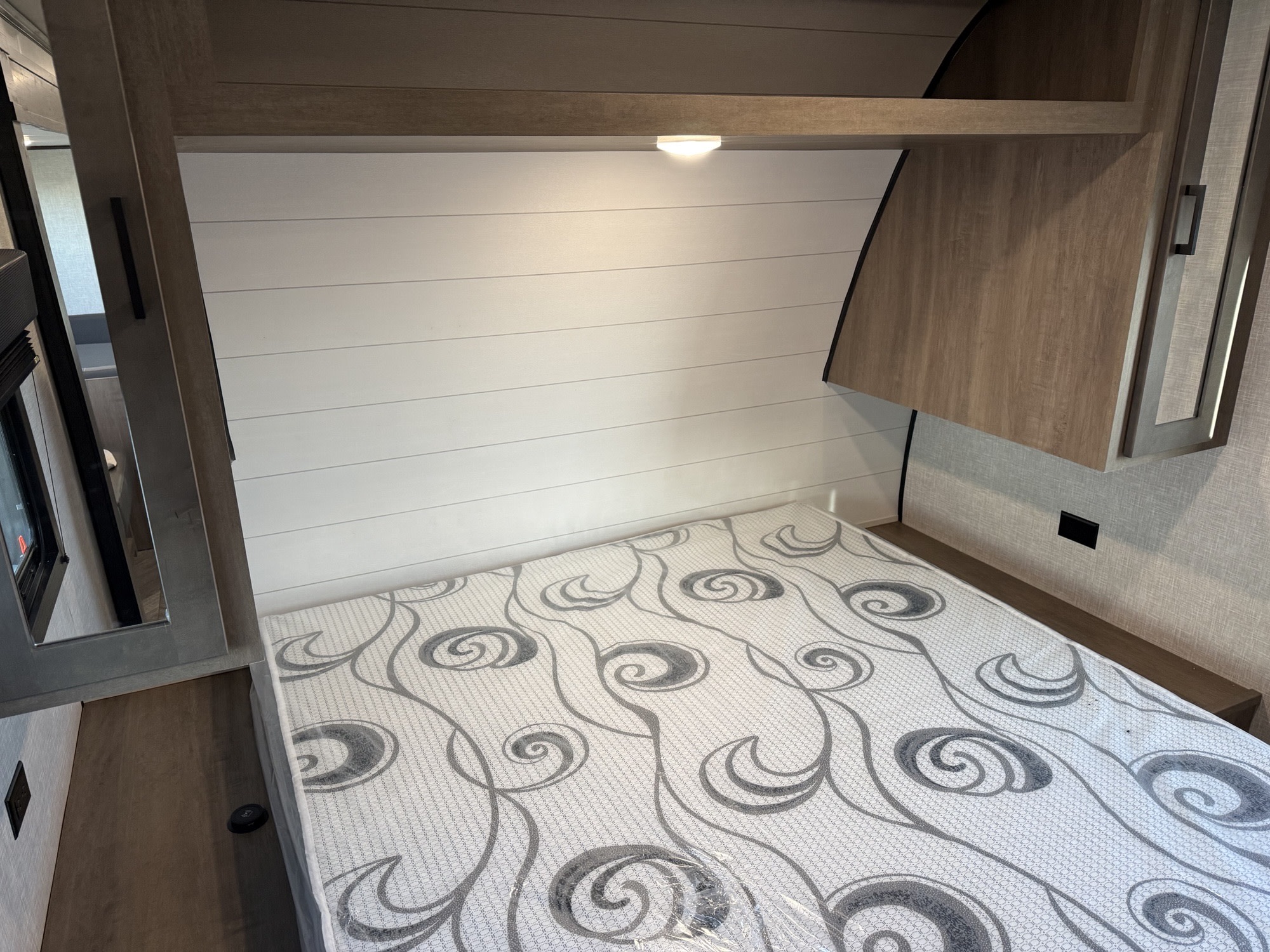 Modern RV rental bedroom with white shiplap headboard, patterned mattress, overhead light, and wood storage.. Starcraft Autumn Ridge 2024