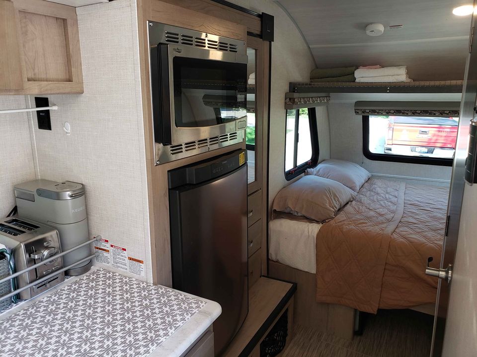 Compact rv rental interior showing a cozy kitchen with microwave, fridge, toaster, and a comfortable bed area with windows.. R-Pod R-Pod Trailer 2020