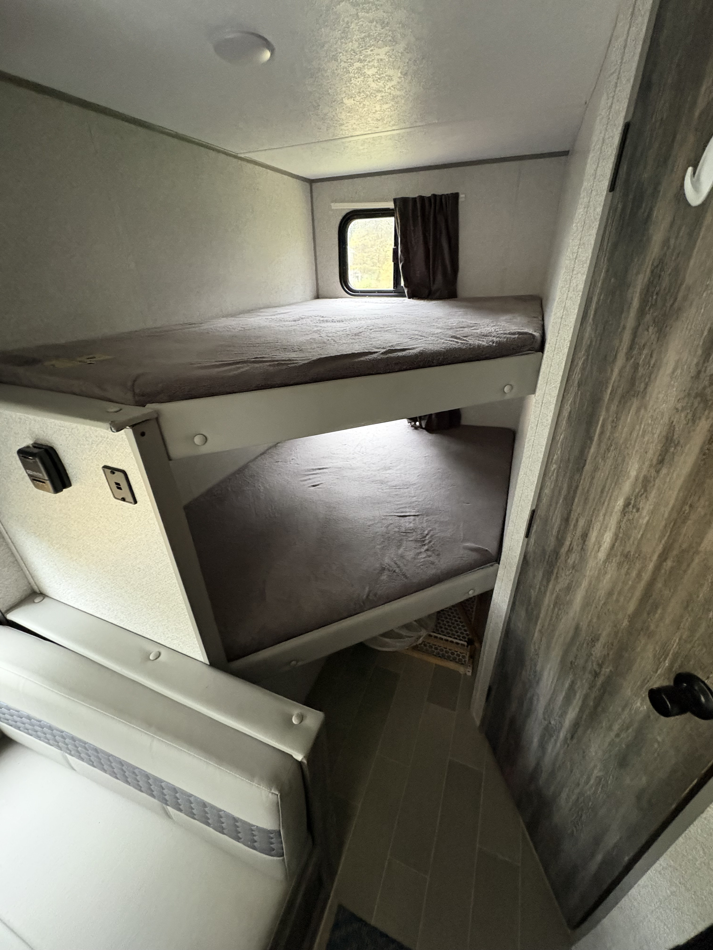 Cozy RV rental sleeping area featuring two bunk beds with grey bedding, a window, and an adjacent sofa.. Forest River Wildwood FSX 2019