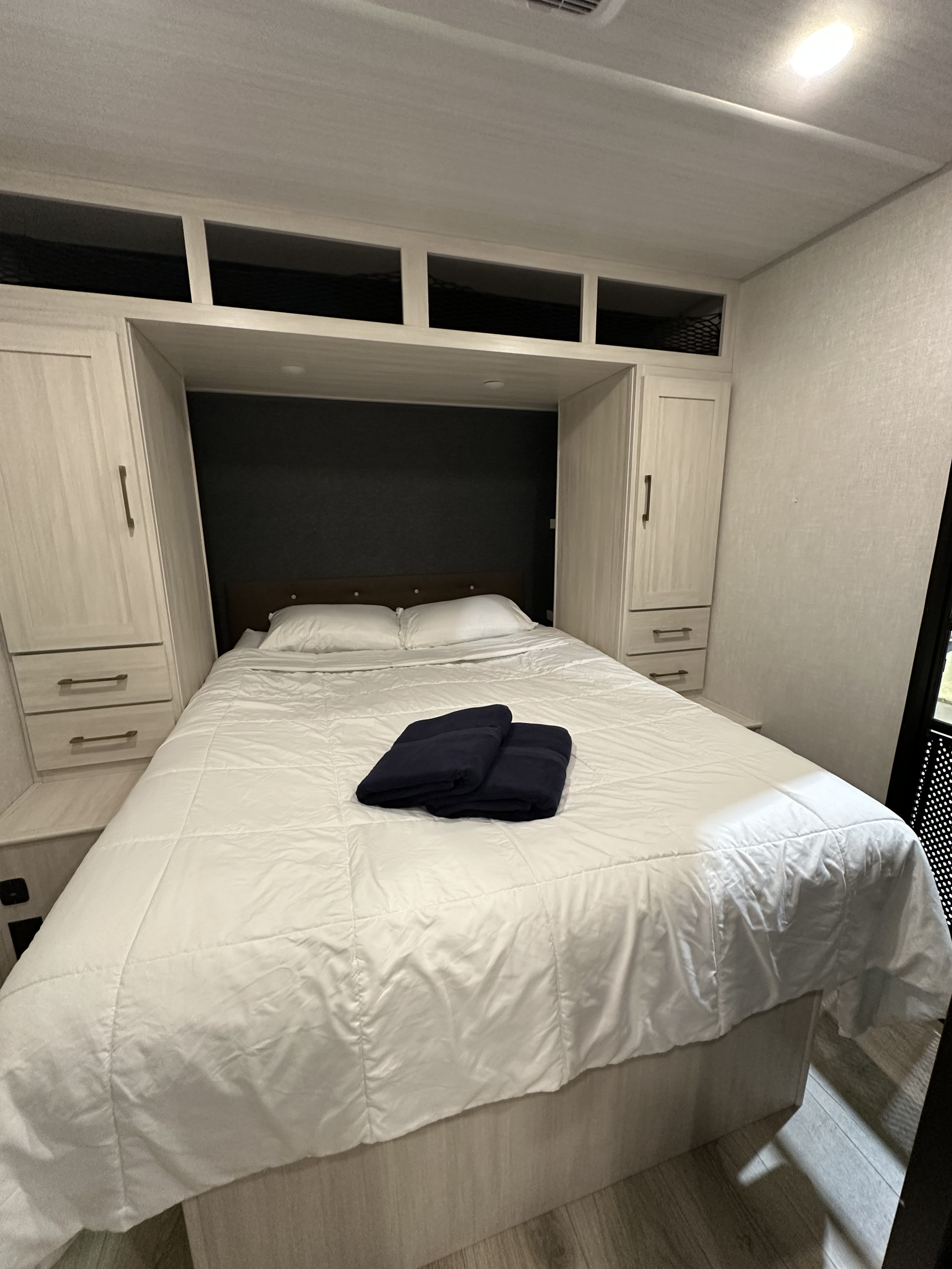 This inviting RV rental bedroom features a crisp white bed, built-in light wood storage, and a dark headboard.. Forest River Surveyor 2026