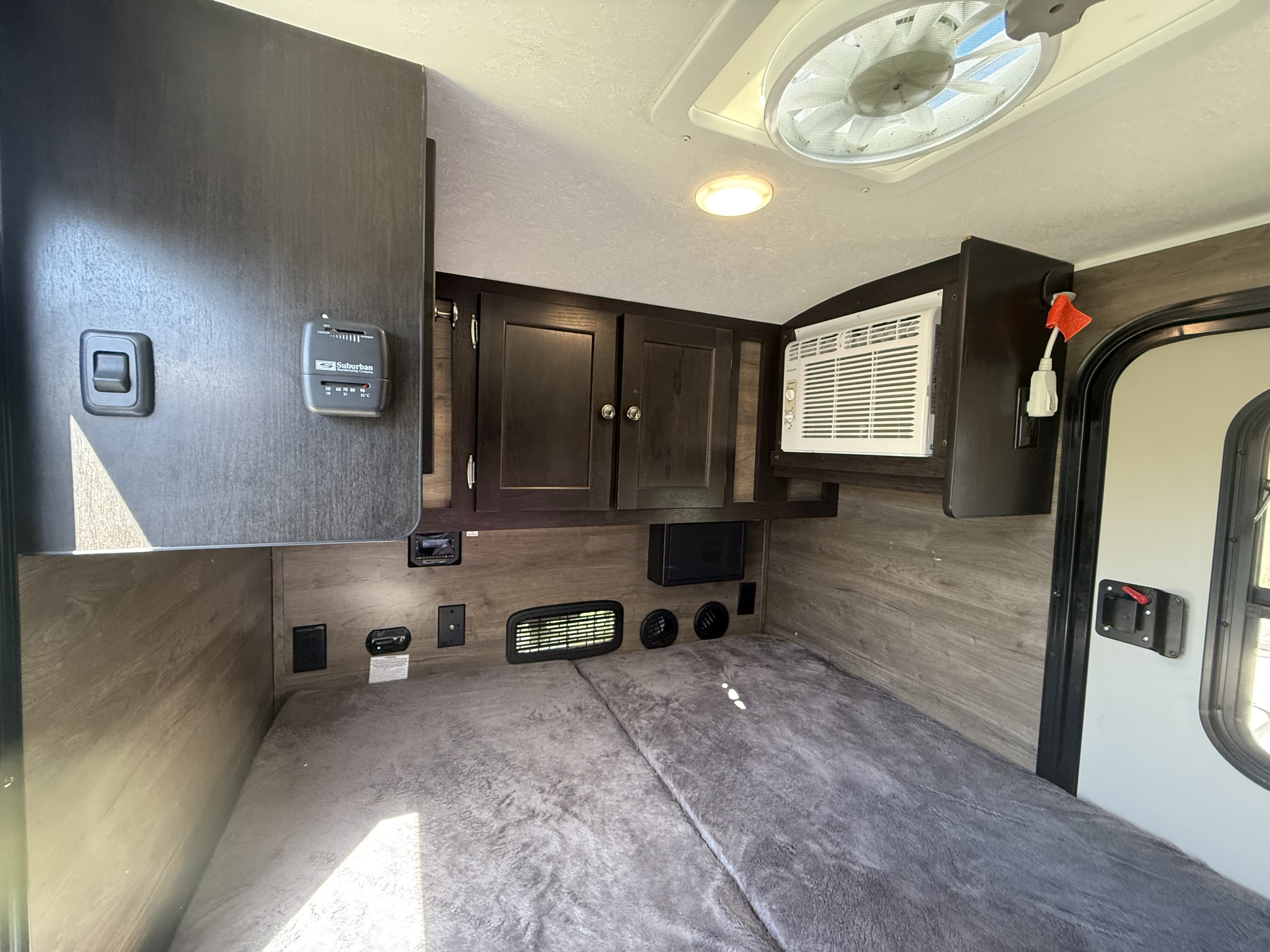 RV rental interior: a compact sleeping area with dark wood cabinets, AC, and a Suburban thermostat.. Braxton Creek Bushwhacker 2022